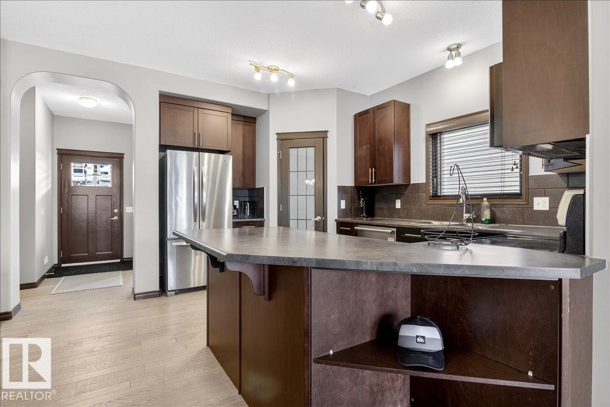 The kitchen features rich wood cabinetry, stainless steel appliances, and a spacious island with a dark countertop - 1530 Chapman Way, Edmonton, AB - Indoor Photo Showing Kitchen With Stainless Steel Kitchen