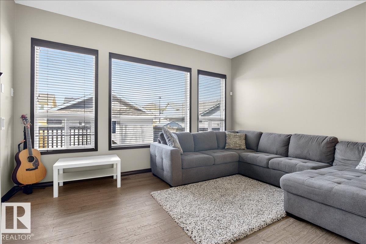 Living area featuring three large windows with blinds, light-colored walls, and wood-style flooring - 1530 Chapman Way, Edmonton, AB - Indoor Photo Showing Living Room