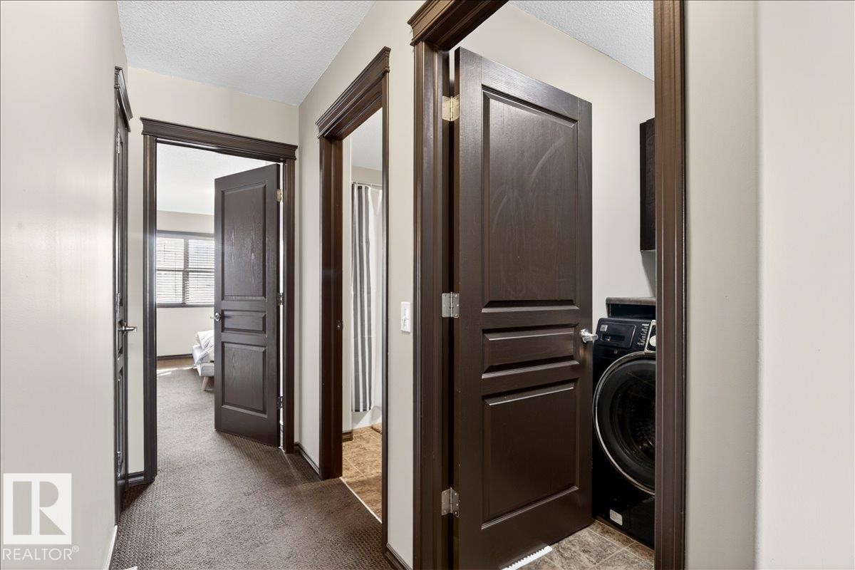 Hallway with dark wood doors, light neutral walls, and dark carpeted flooring - 1530 Chapman Way, Edmonton, AB - Indoor Photo Showing Laundry Room