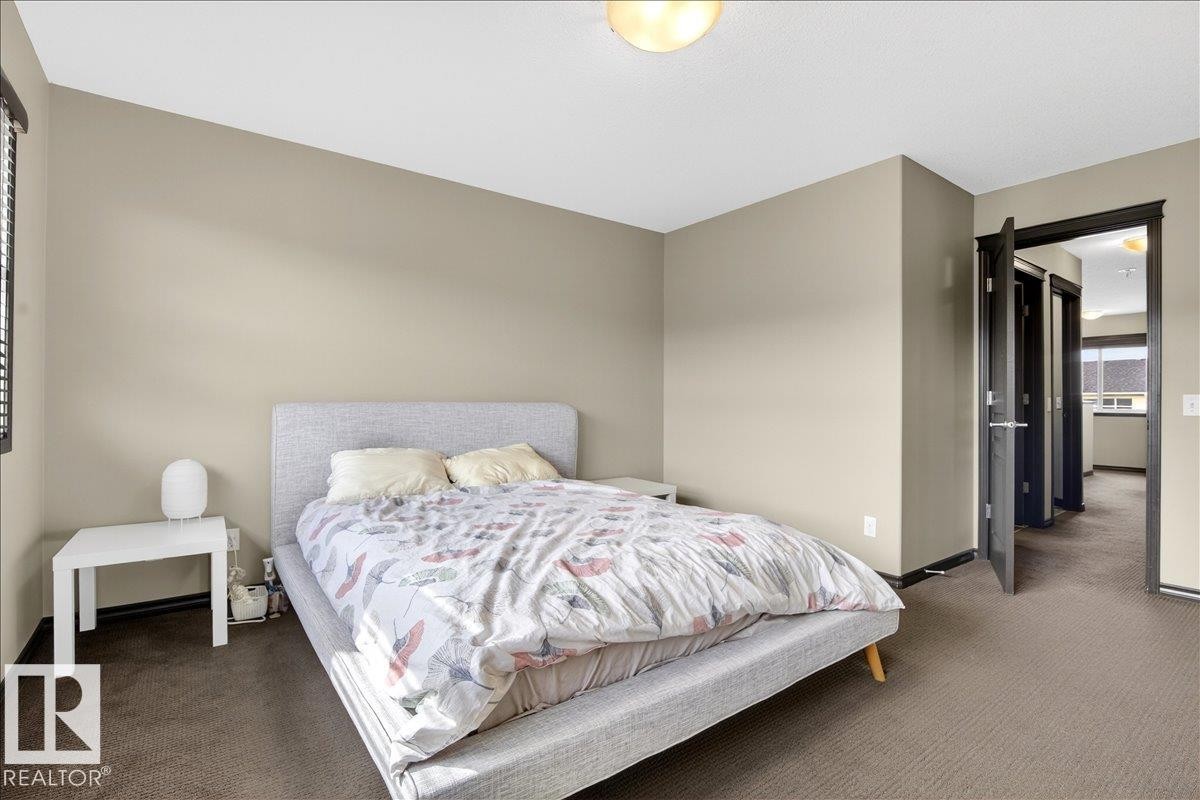 The bedroom features neutral-toned walls and dark carpeting, with a window providing natural light - 1530 Chapman Way, Edmonton, AB - Indoor Photo Showing Bedroom