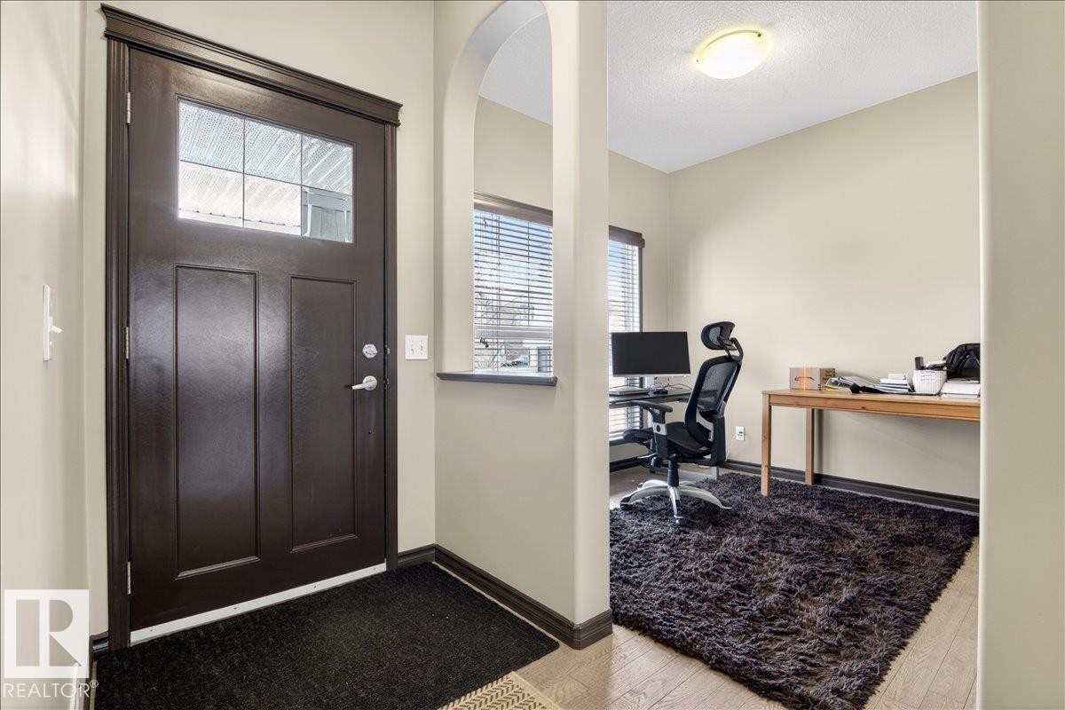 Inviting entryway with a dark wood door featuring a window panel, leading into a room with light-colored walls and a window with blinds - 1530 Chapman Way, Edmonton, AB - Indoor