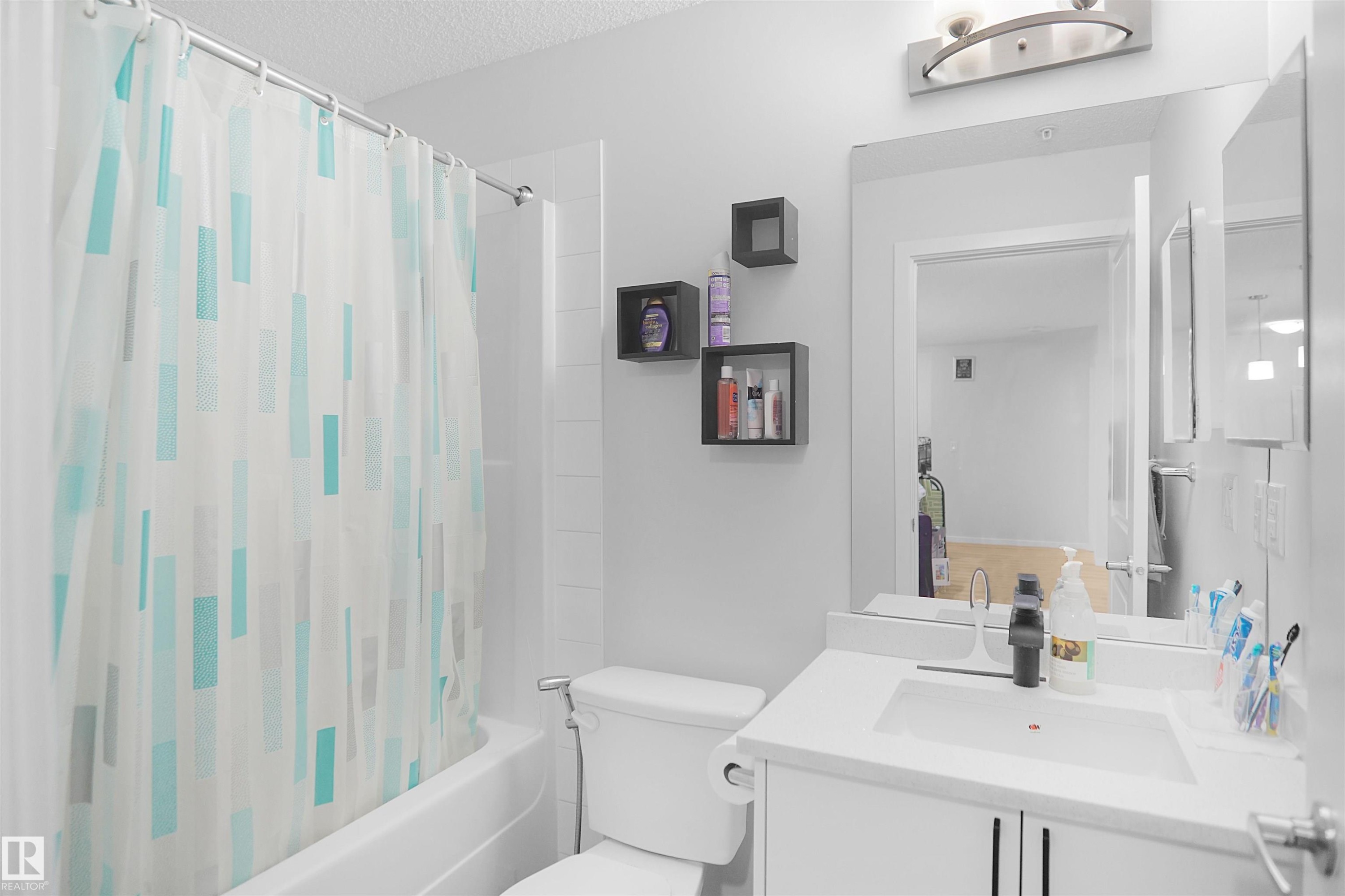 The bathroom features a white vanity with an integrated sink, a large mirror, and a combined shower and tub - 103 3353 16A Avenue, Edmonton, AB - Indoor Photo Showing Bathroom