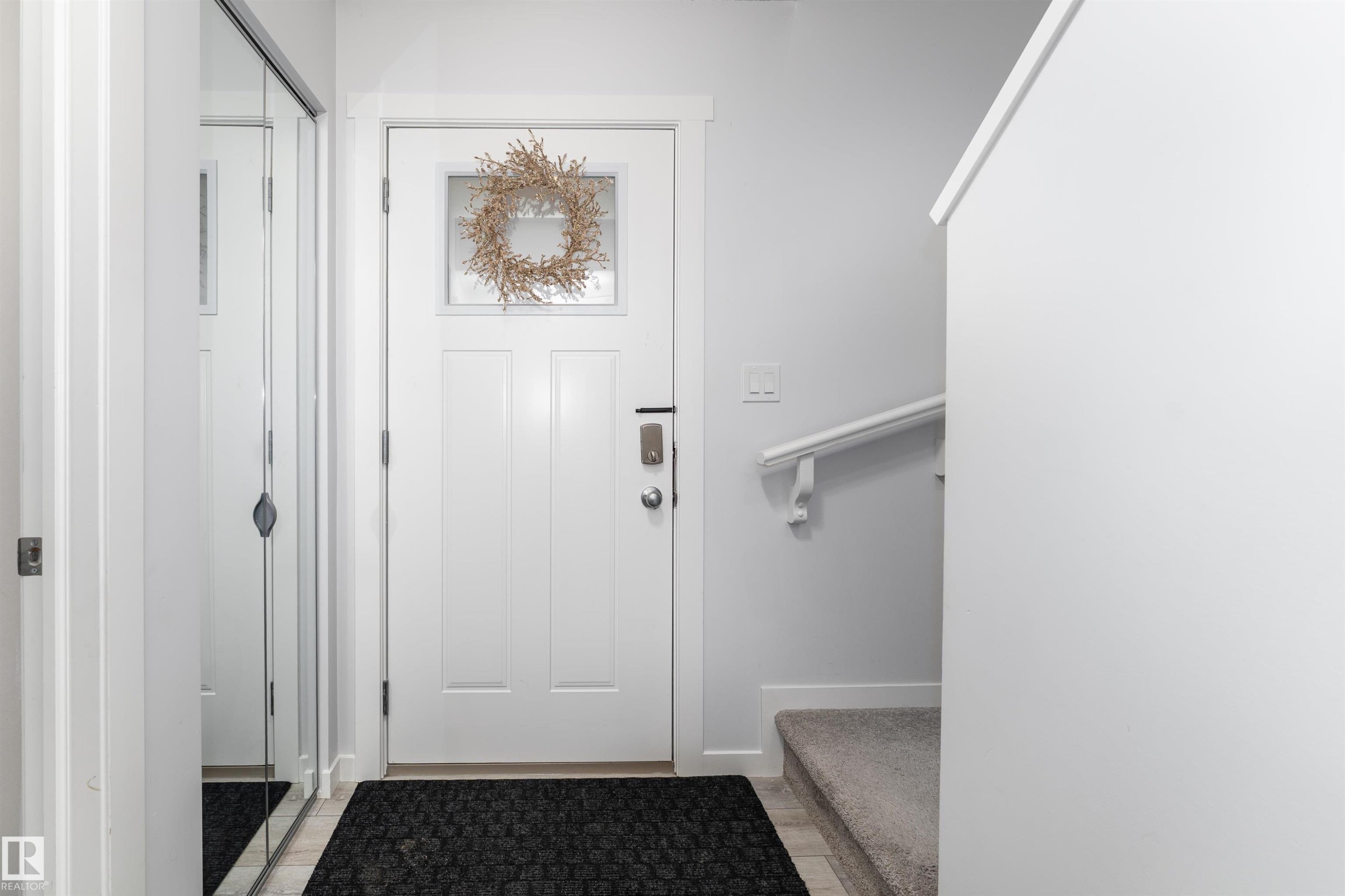 Entryway featuring a white door with a window, a mirrored closet door, and a carpeted stairwell - 6 12815 Cumberland Rd, Edmonton, AB - Indoor Photo Showing Other Room