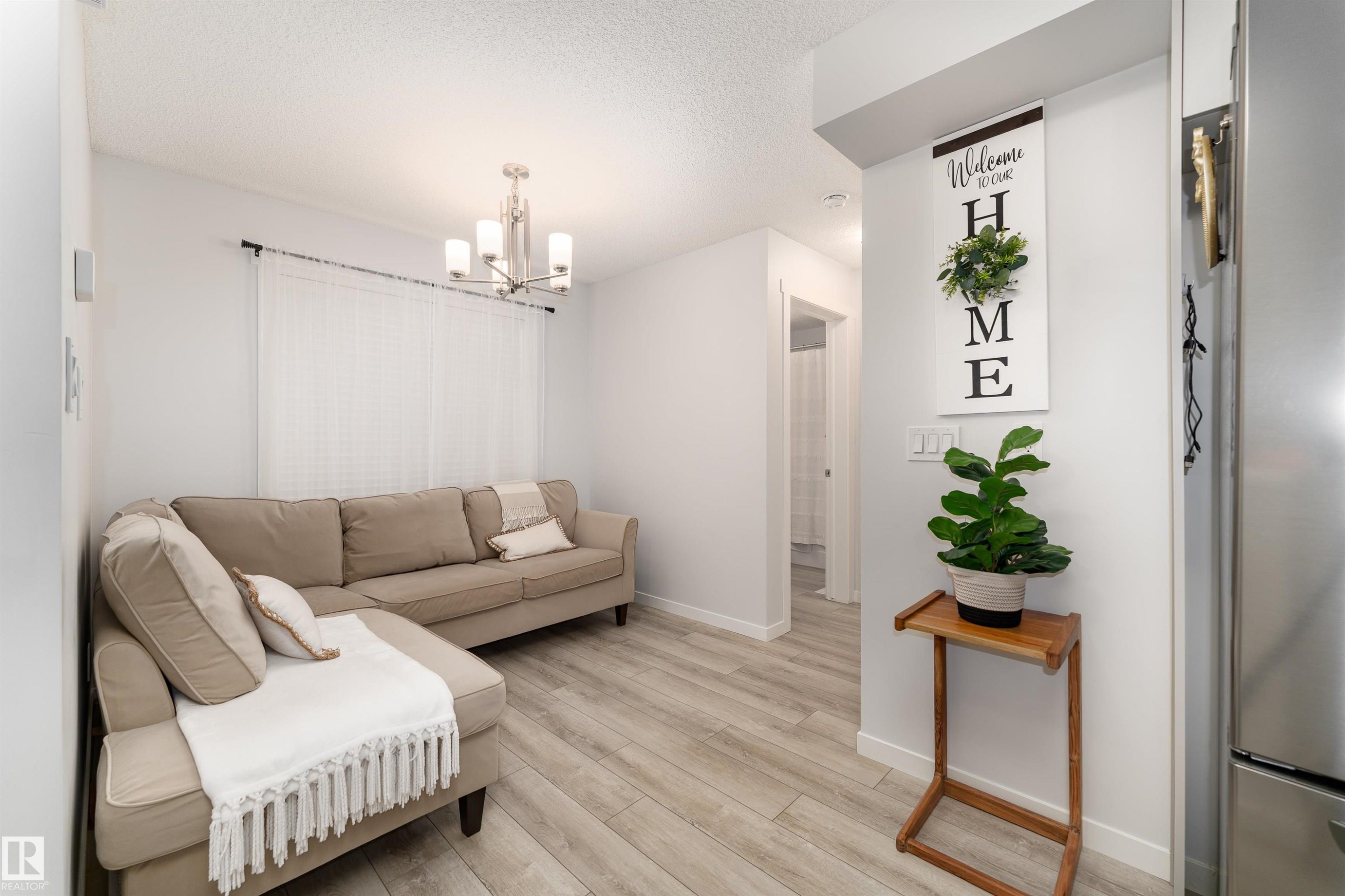 The living area features light-toned flooring, white walls, and a contemporary chandelier - 6 12815 Cumberland Rd, Edmonton, AB - Indoor
