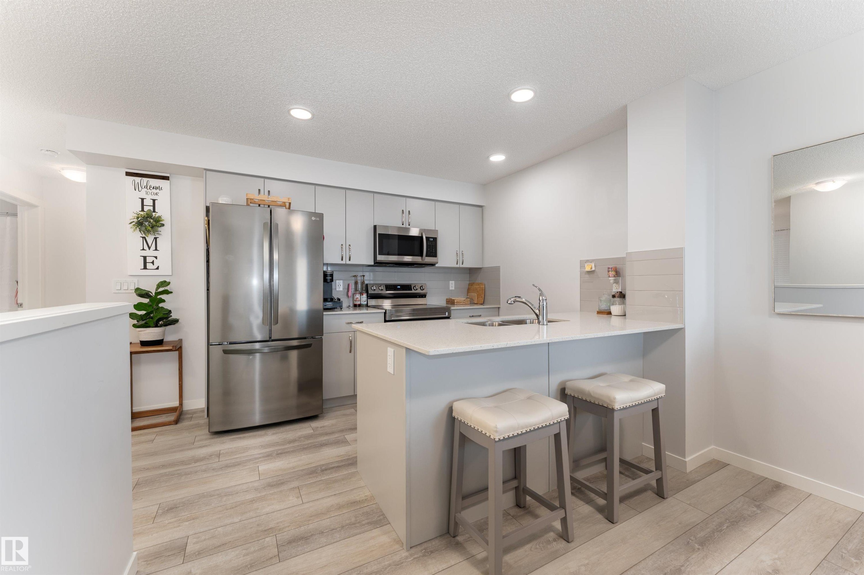 The kitchen features light-toned flooring, grey cabinetry, and a light-colored countertop - 6 12815 Cumberland Rd, Edmonton, AB - Indoor Photo Showing Kitchen
