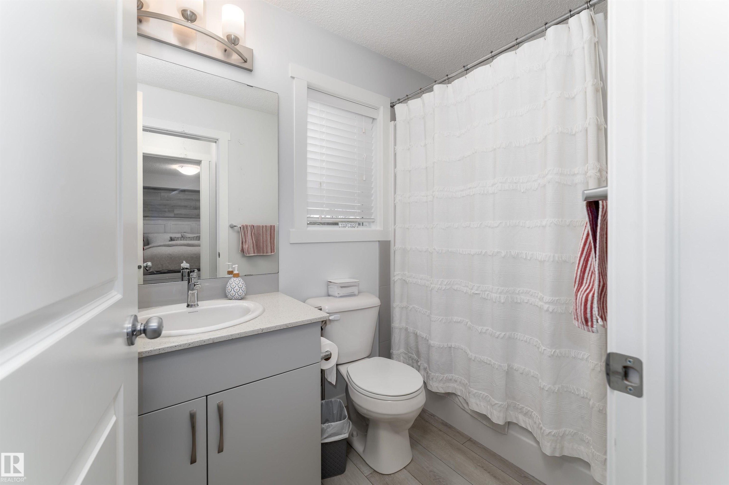 Bathroom featuring a vanity with a light gray cabinet and a sink, a toilet, and a shower with a white curtain - 6 12815 Cumberland Rd, Edmonton, AB - Indoor Photo Showing Bathroom