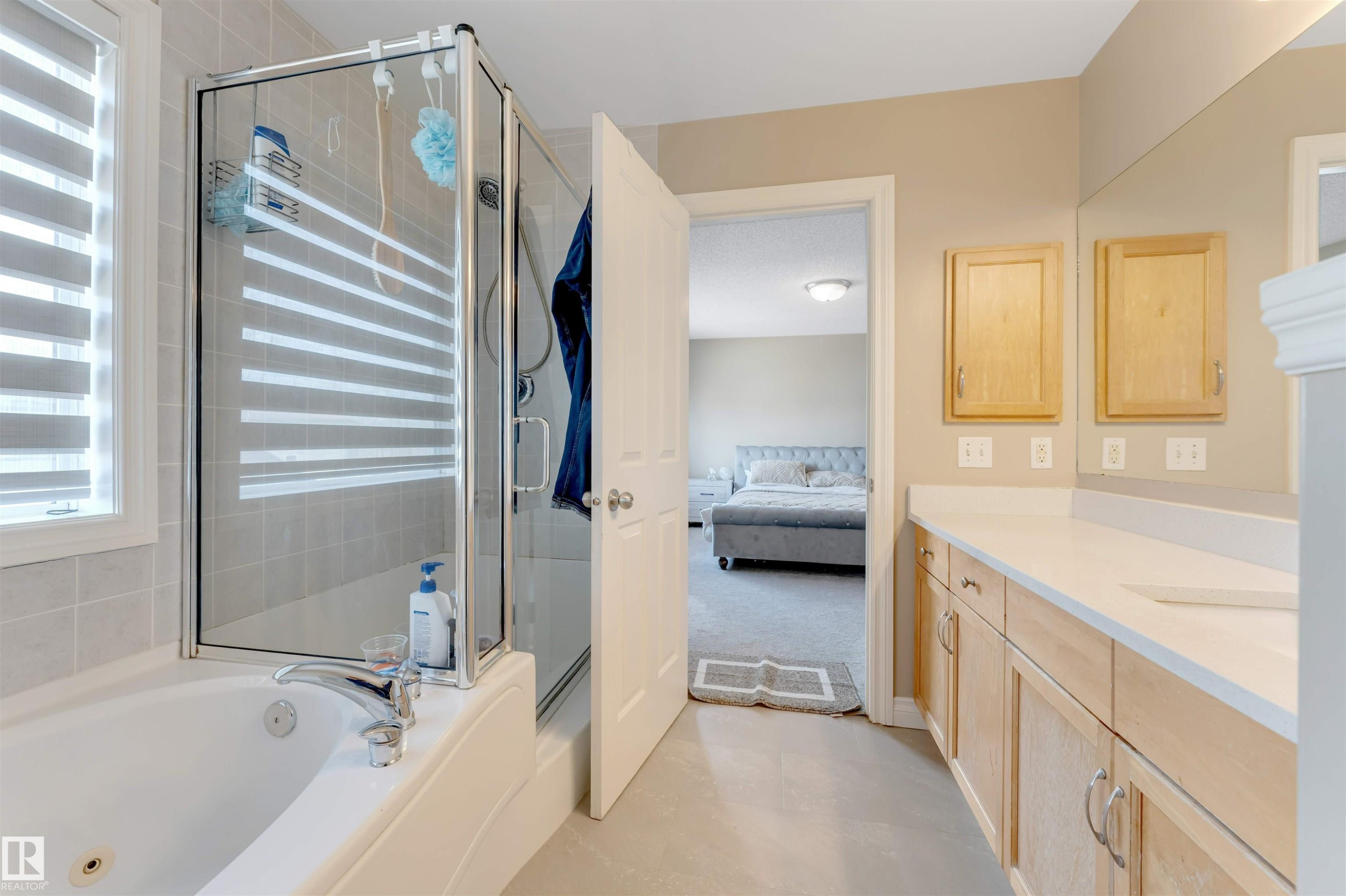 This bathroom features a bathtub with a shower enclosure, a window with blinds, and a vanity with a light-colored countertop and wooden cabinetry - 121 64 Street, Edmonton, AB - Indoor Photo Showing Bathroom