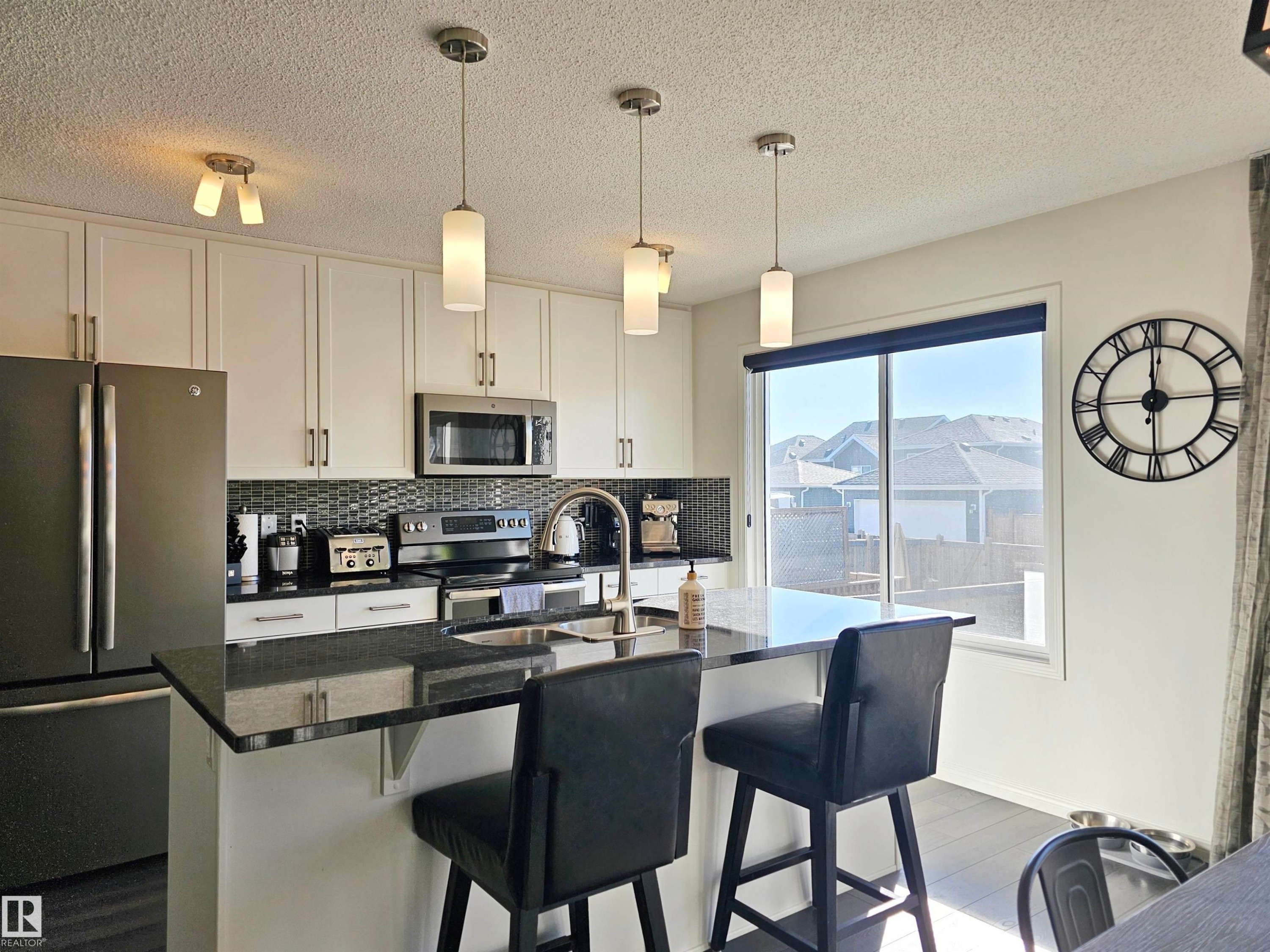 The kitchen features white cabinetry, stainless steel appliances, and a dark stone countertop with a breakfast bar - 6888 Evans Wynd, Edmonton, AB - Indoor Photo Showing Kitchen With Stainless Steel Kitchen With Upgraded Kitchen