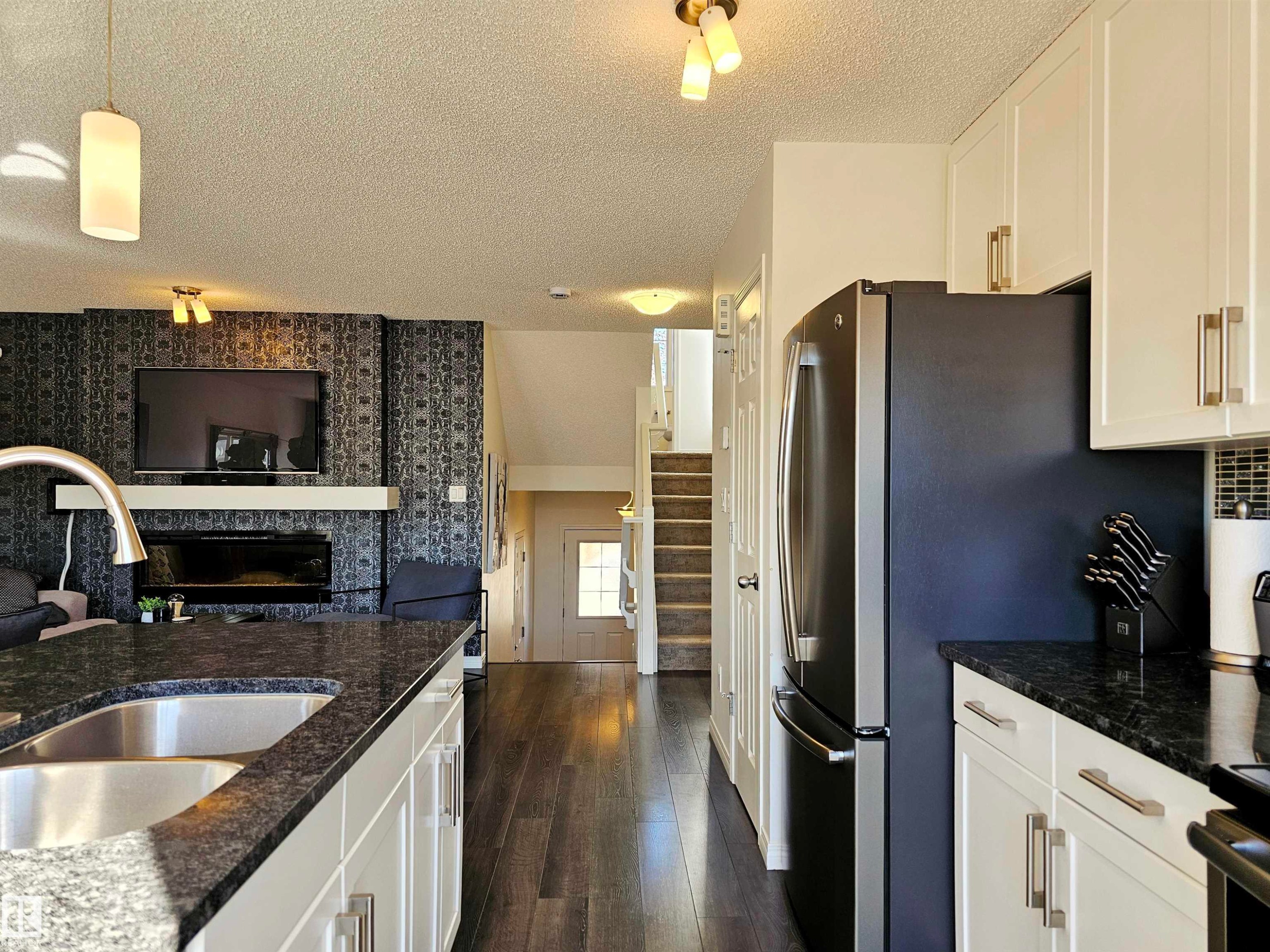 The kitchen features white cabinetry, dark countertops, a stainless steel sink with a gooseneck faucet, and a stainless steel refrigerator - 6888 Evans Wynd, Edmonton, AB - Indoor Photo Showing Kitchen With Double Sink