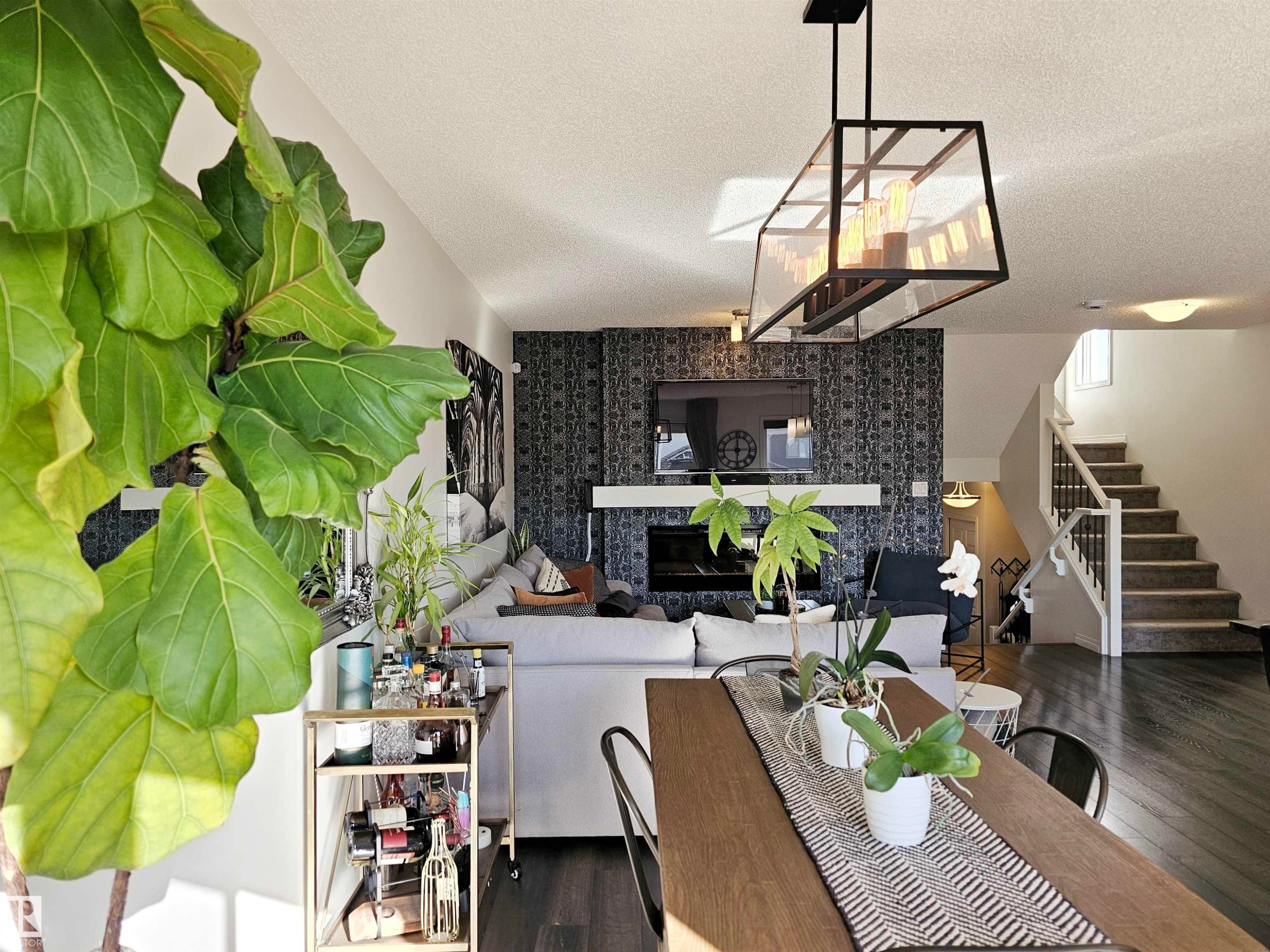 The open concept living area features dark hardwood flooring, a fireplace with a white mantel, and a stylish chandelier - 6888 Evans Wynd, Edmonton, AB - Indoor Photo Showing Dining Room