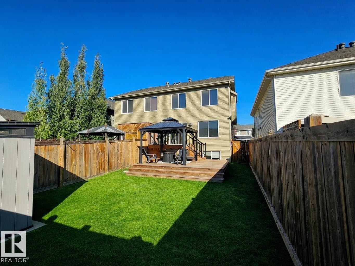 The property features a spacious backyard with a well-maintained lawn and a wooden fence - 6888 Evans Wynd, Edmonton, AB - Outdoor With Deck Patio Veranda