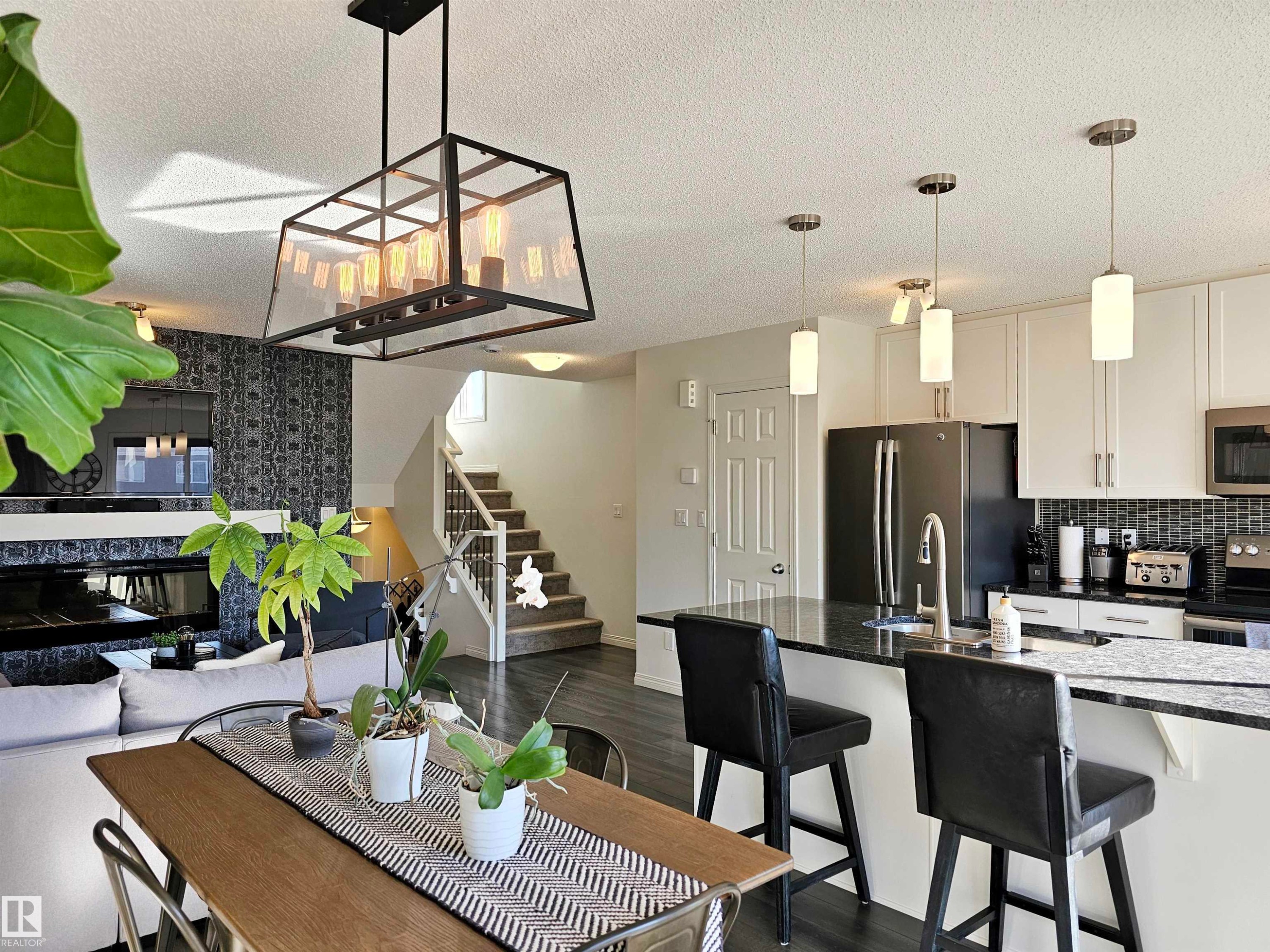Open concept living area with dark flooring, a modern chandelier, and a prominent staircase - 6888 Evans Wynd, Edmonton, AB - Indoor