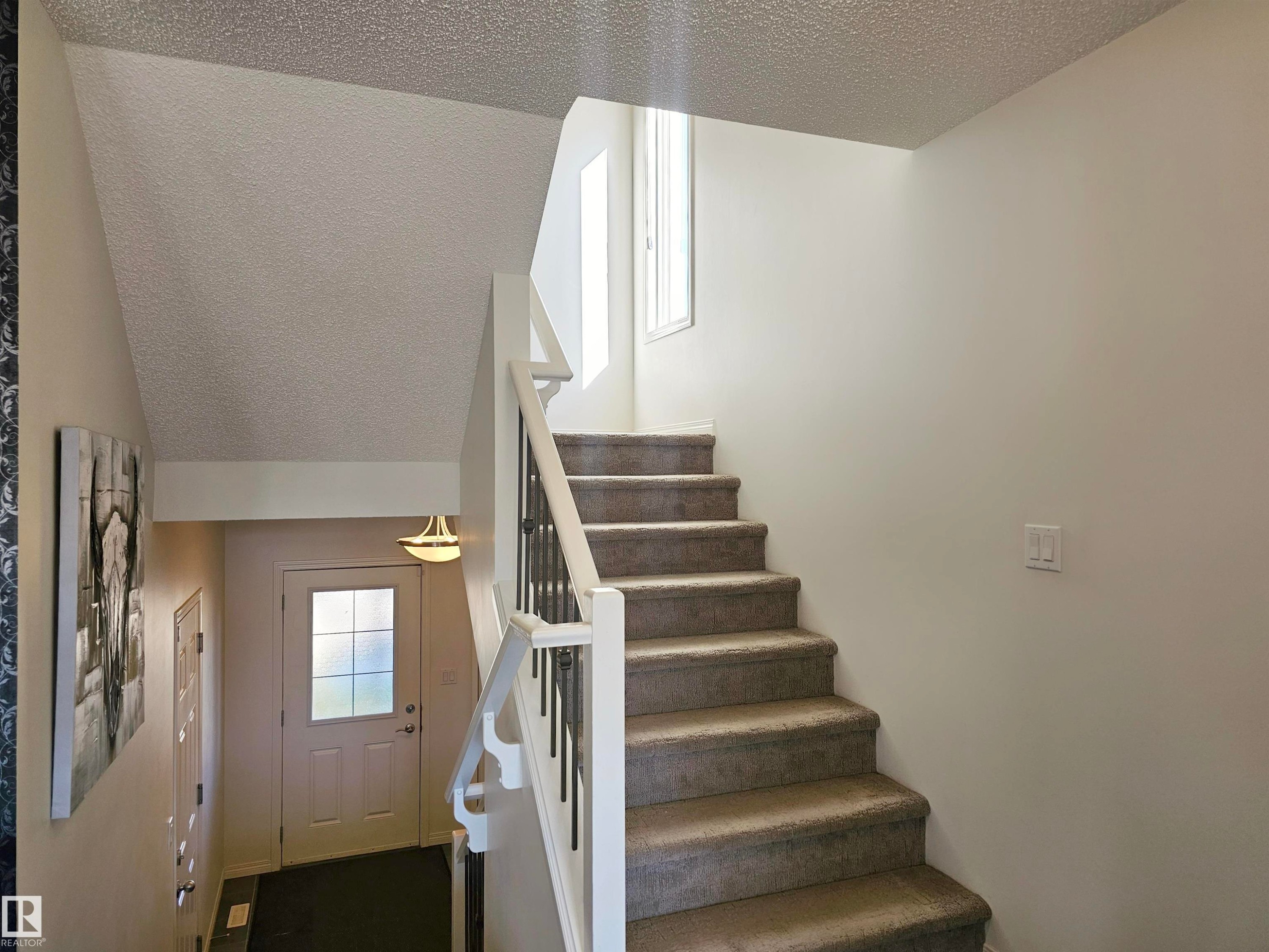 The property features a staircase with carpeted steps and a white railing, a white door with frosted glass panels, and a ceiling light fixture - 6888 Evans Wynd, Edmonton, AB - Indoor Photo Showing Other Room