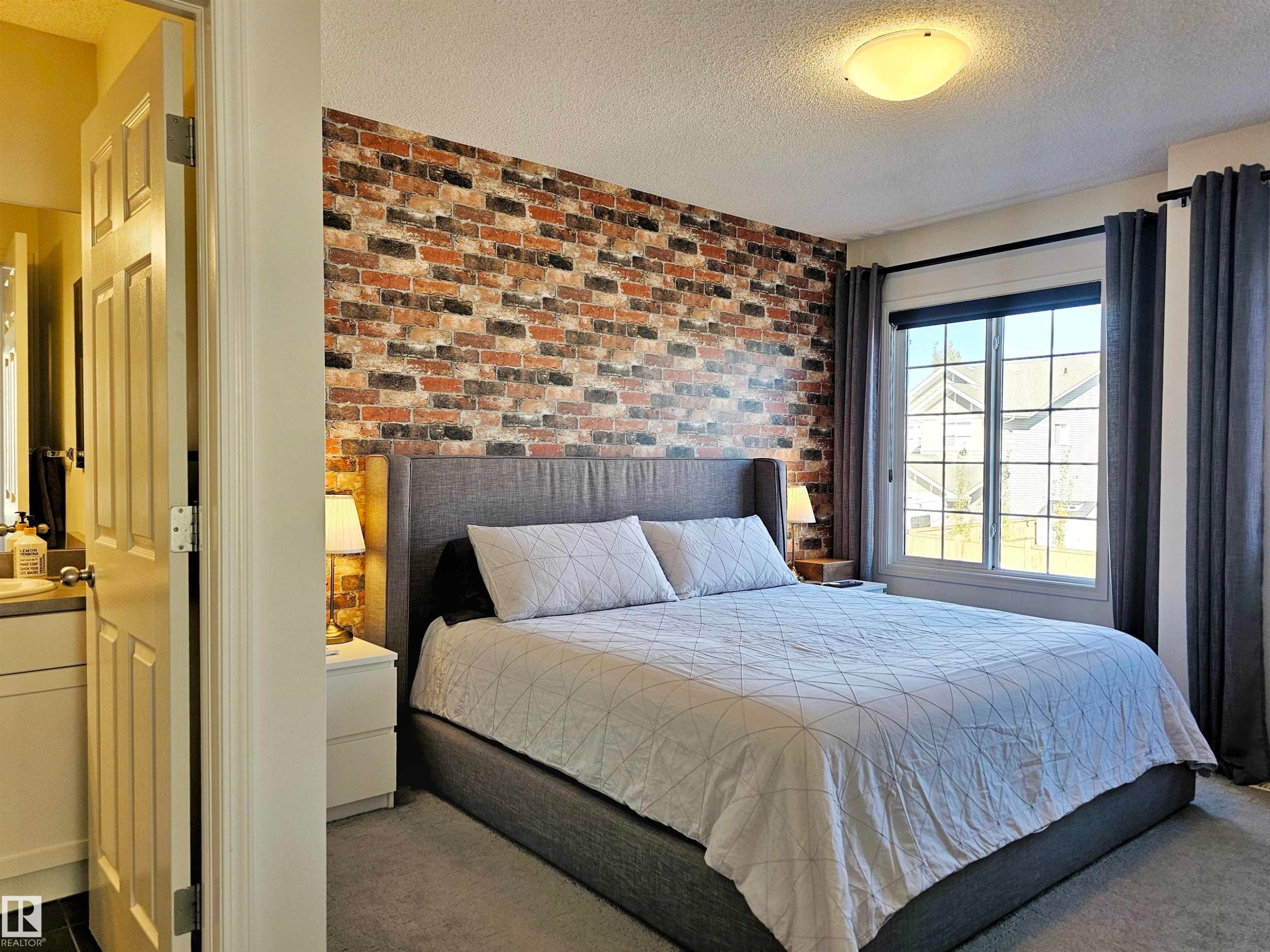 This room features a textured brick accent wall, carpeted flooring, and a large window with privacy blinds and drapes - 6888 Evans Wynd, Edmonton, AB - Indoor Photo Showing Bedroom