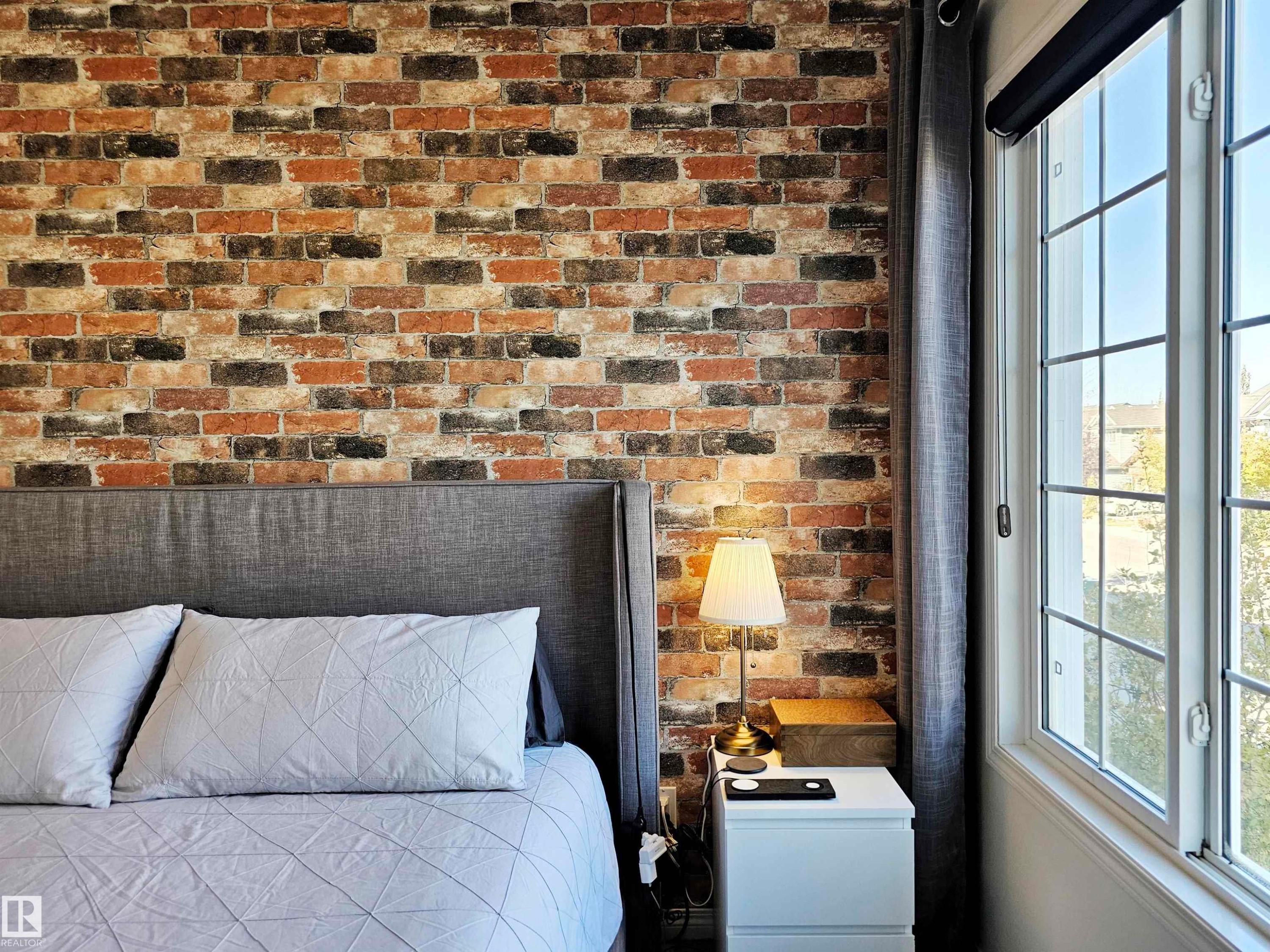 The property features an exposed brick accent wall and a window with grilles providing natural light - 6888 Evans Wynd, Edmonton, AB - Indoor