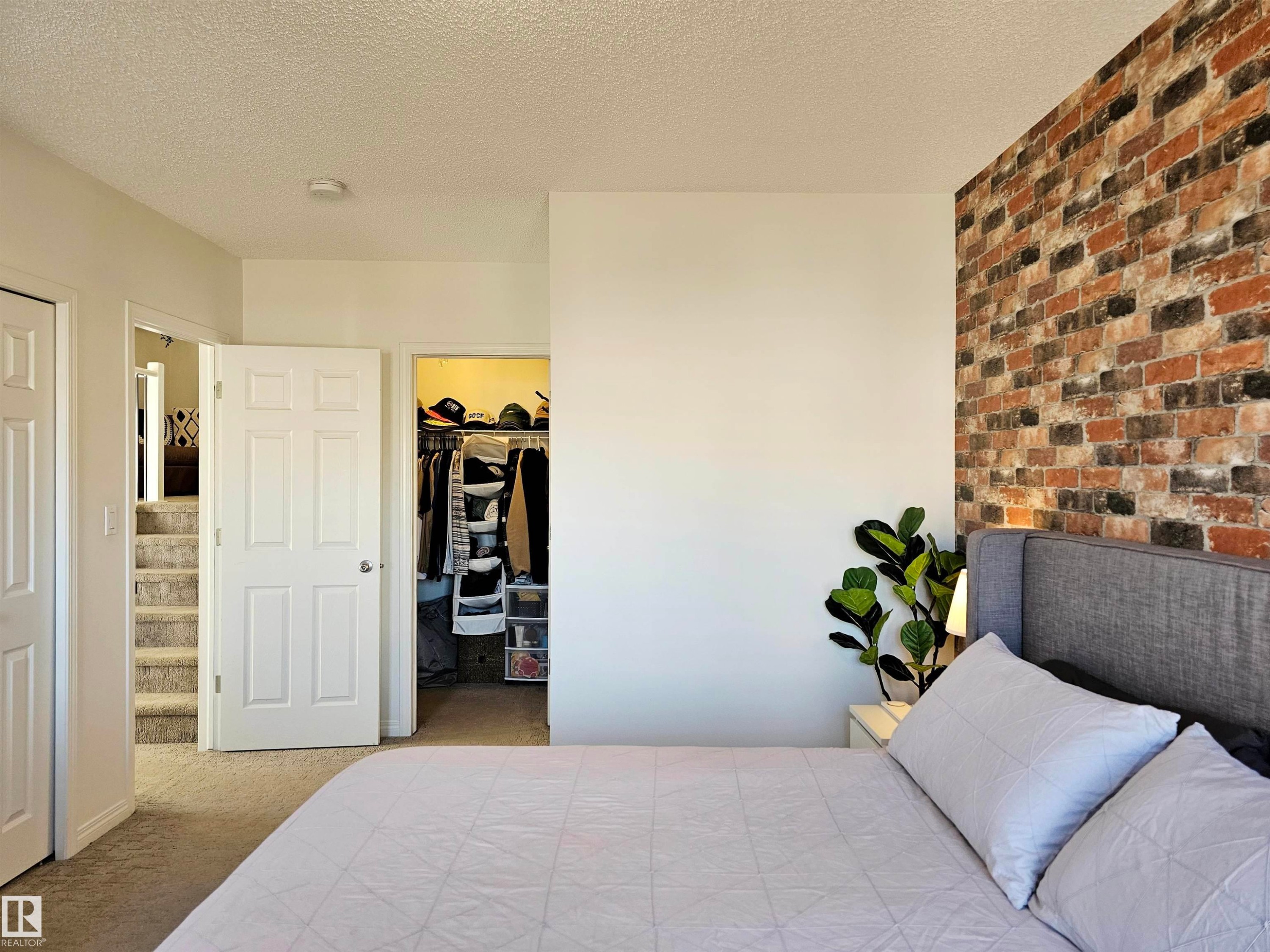 The bedroom features a textured brick accent wall, carpeted flooring, and a closet with a built-in storage system - 6888 Evans Wynd, Edmonton, AB - Indoor Photo Showing Bedroom