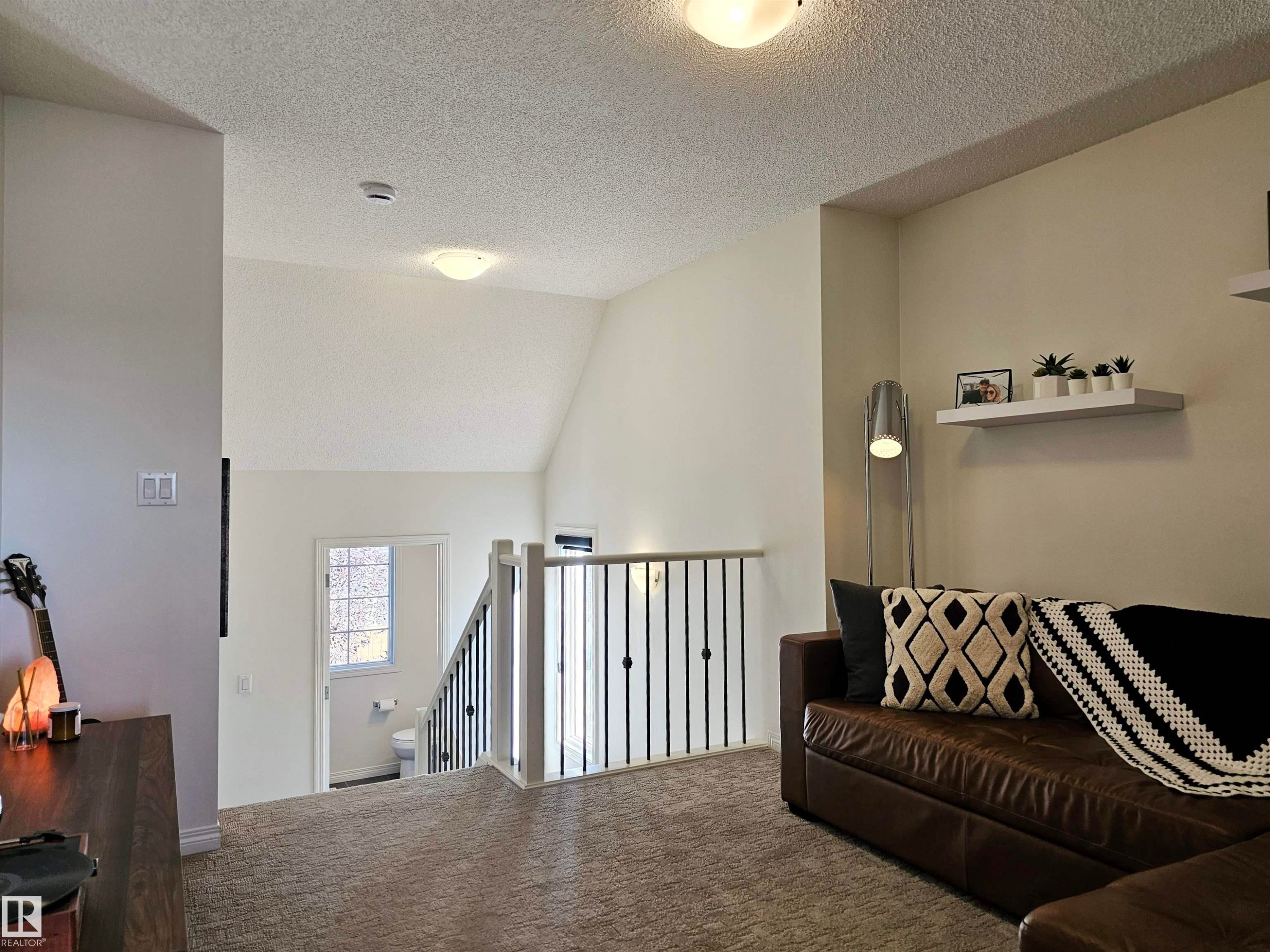 This spacious living area features vaulted ceilings, a carpeted floor, and a metal balustrade - 6888 Evans Wynd, Edmonton, AB - Indoor Photo Showing Other Room