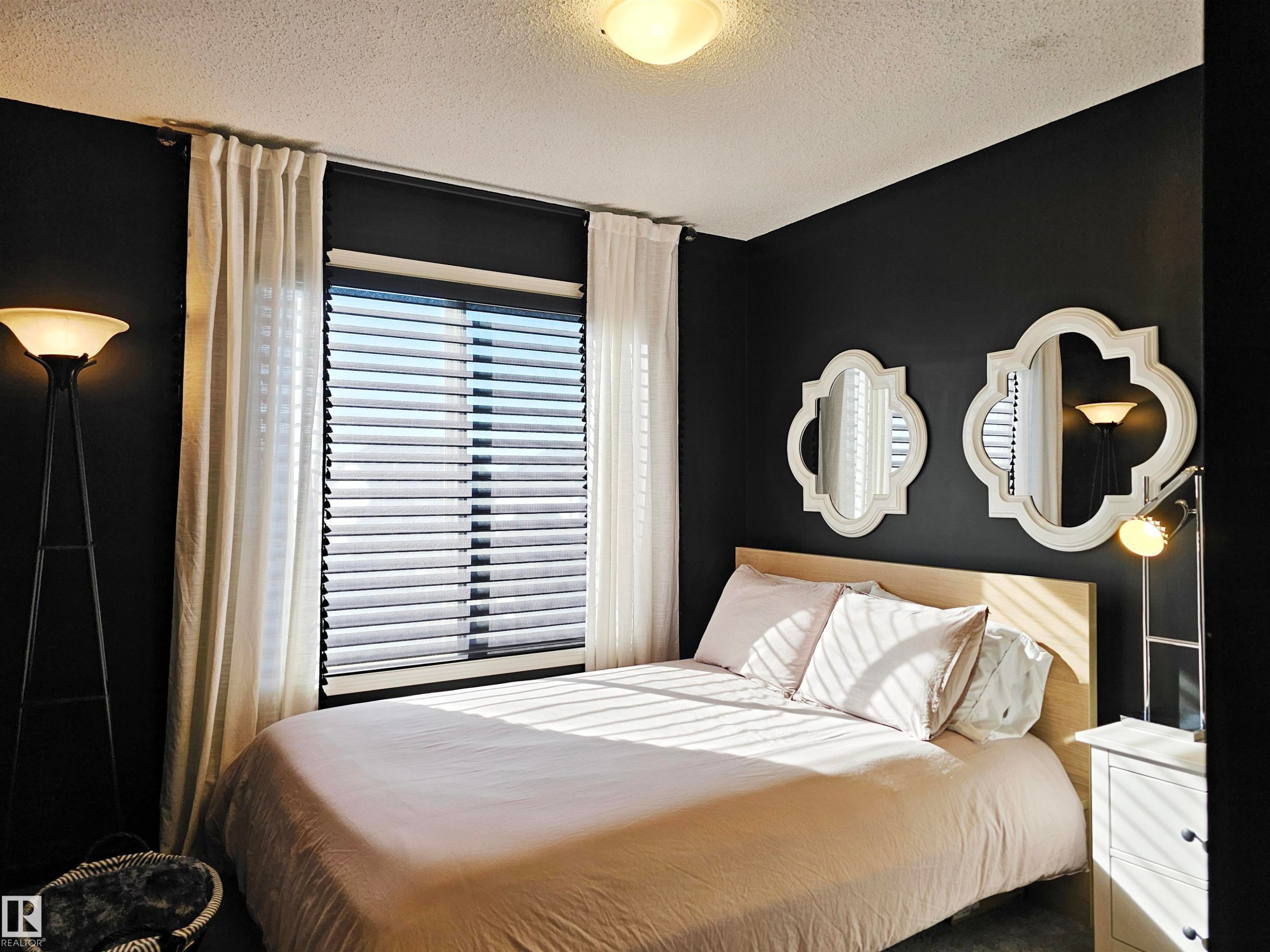 This room features a window with blinds and sheer white curtains, dark wall paint, and a ceiling light fixture - 6888 Evans Wynd, Edmonton, AB - Indoor Photo Showing Bedroom