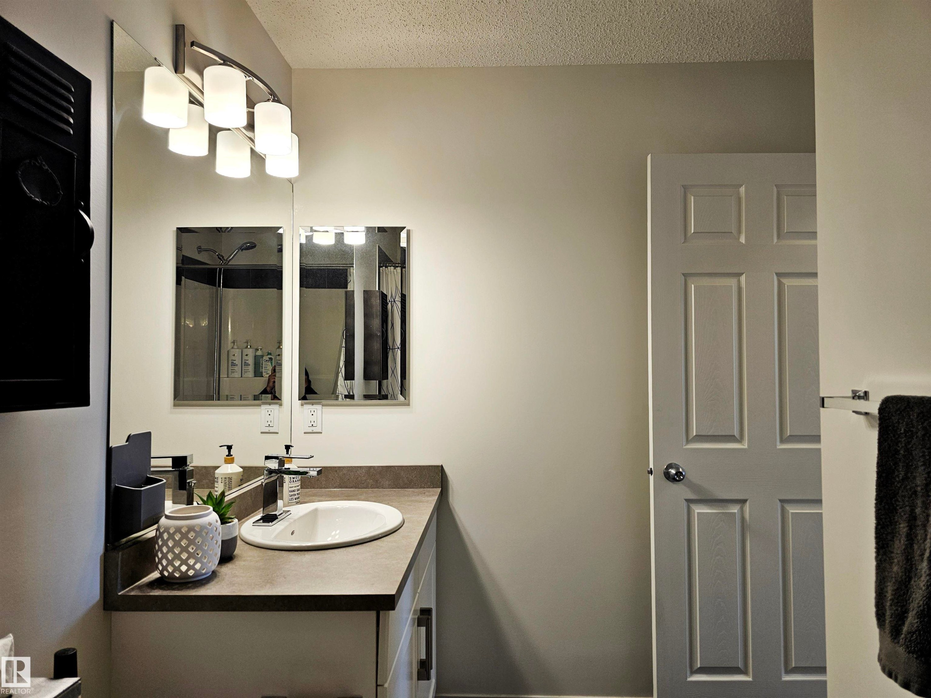 Bathroom featuring a vanity with an oval sink, a wall-mounted light fixture, and a mirrored wall - 6888 Evans Wynd, Edmonton, AB - Indoor Photo Showing Bathroom