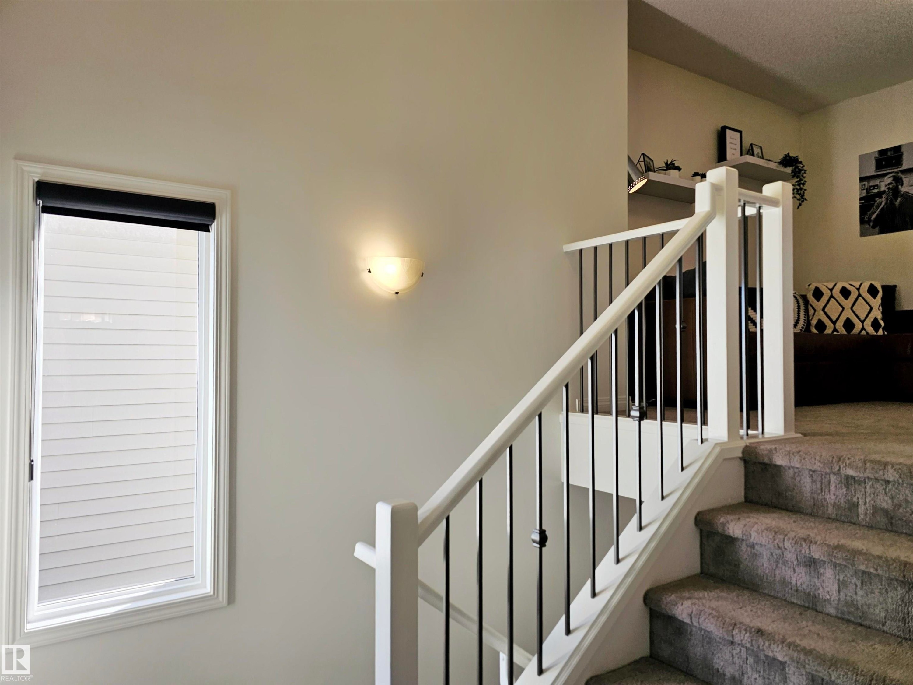 A well-lit staircase featuring carpeted steps and a white railing with black metal spindles - 6888 Evans Wynd, Edmonton, AB - Indoor Photo Showing Other Room