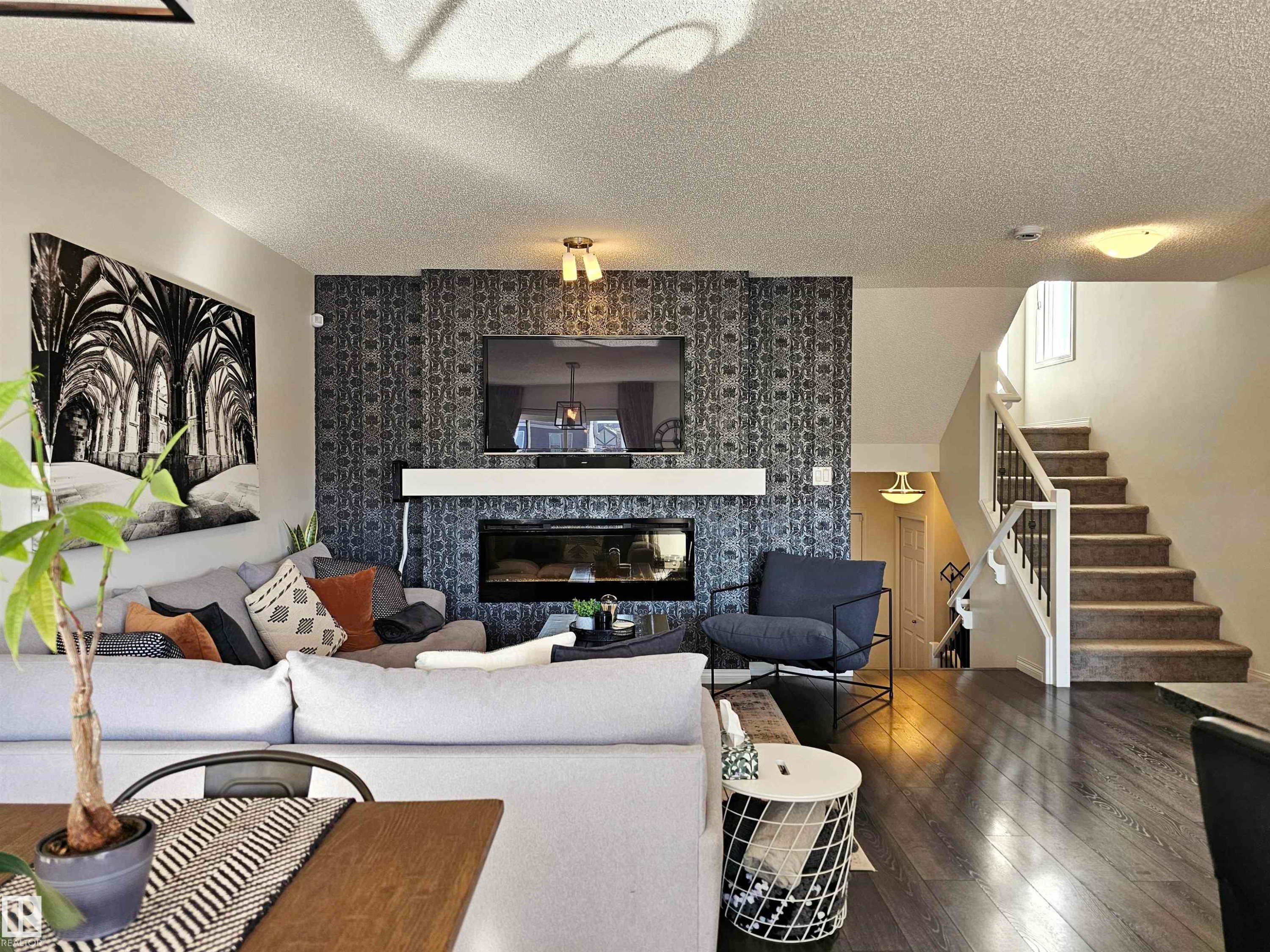 The living area features dark wood flooring, a fireplace with a decorative accent wall, and a staircase with white risers and dark banisters - 6888 Evans Wynd, Edmonton, AB - Indoor Photo Showing Living Room With Fireplace