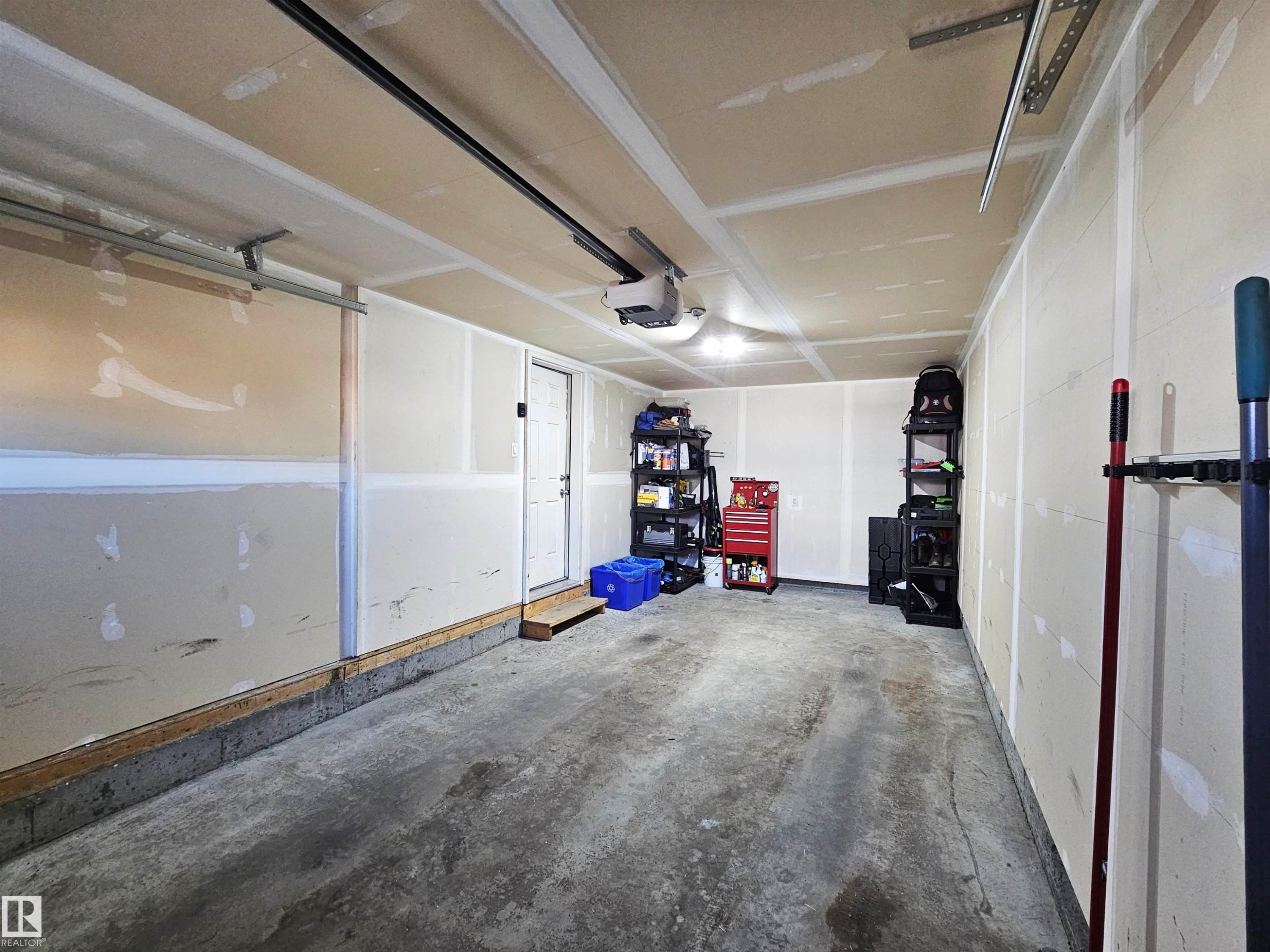 The property includes a spacious garage with a concrete floor, a white utility door, and overhead lighting - 6888 Evans Wynd, Edmonton, AB - Indoor Photo Showing Garage