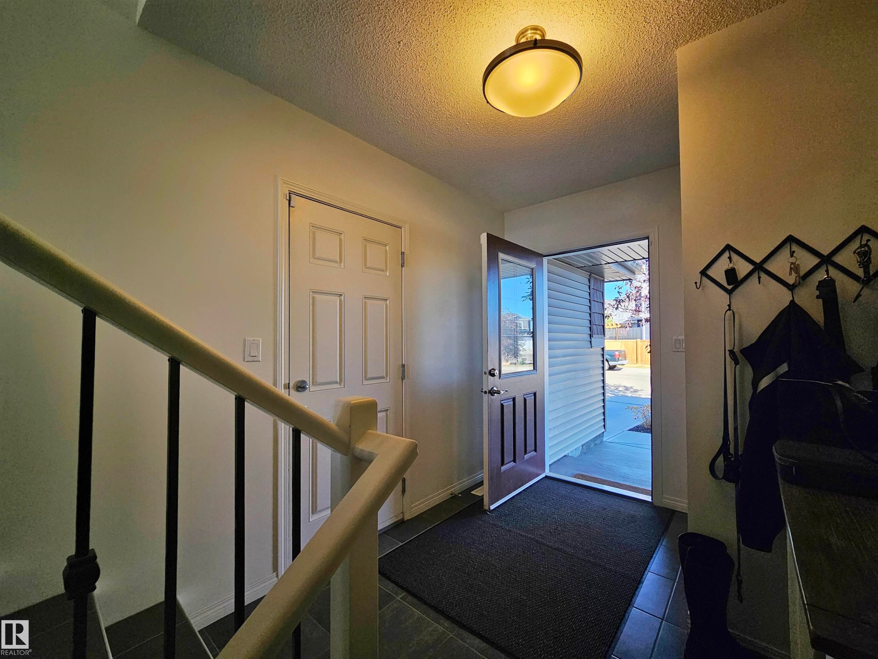 Inviting entryway featuring tile flooring, a light fixture, and a stairway with a light-colored handrail and dark balusters - 6888 Evans Wynd, Edmonton, AB - Indoor Photo Showing Other Room