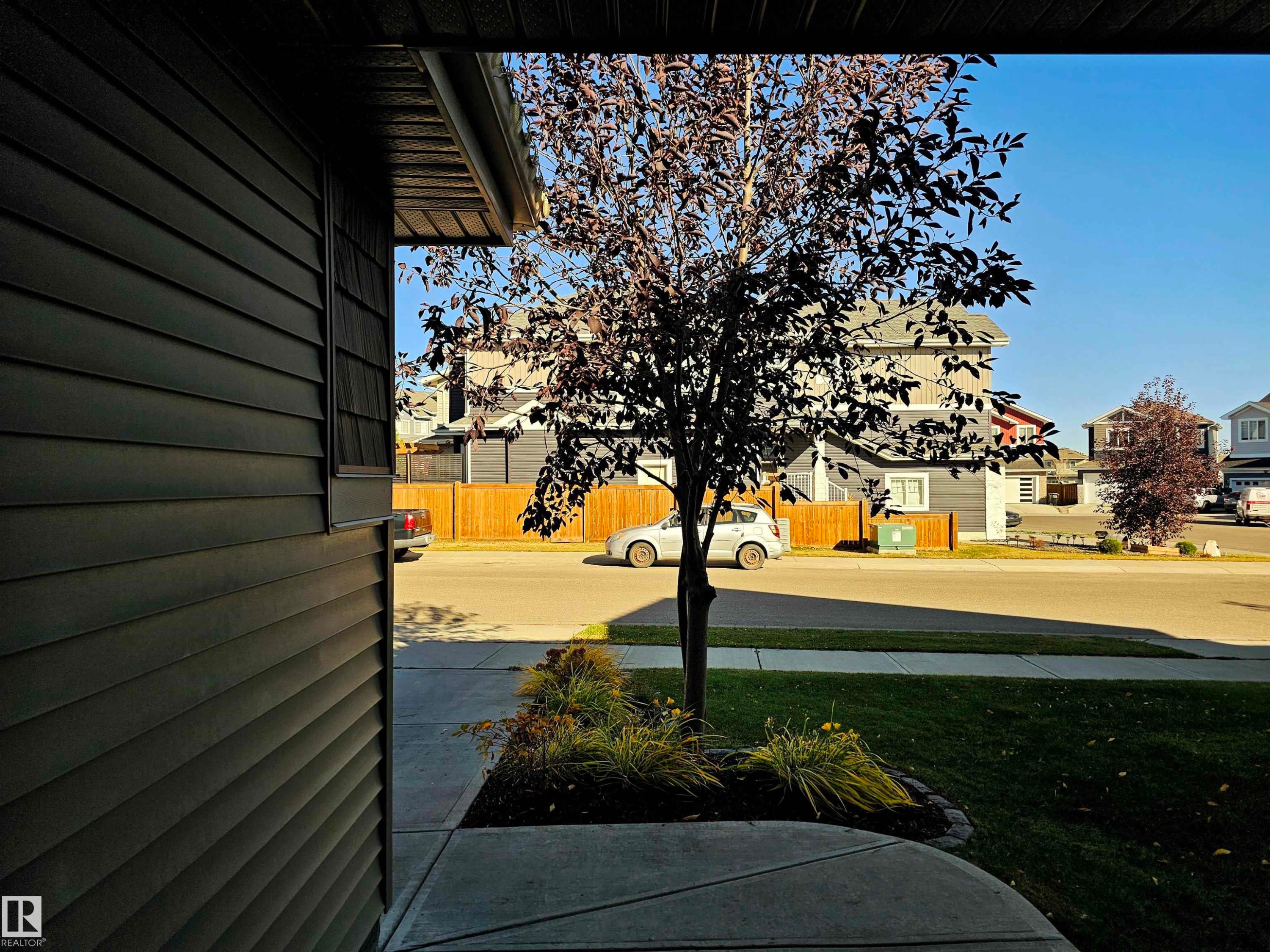 The property features dark-colored horizontal siding, a concrete walkway, and a small tree with dark foliage - 6888 Evans Wynd, Edmonton, AB - Outdoor