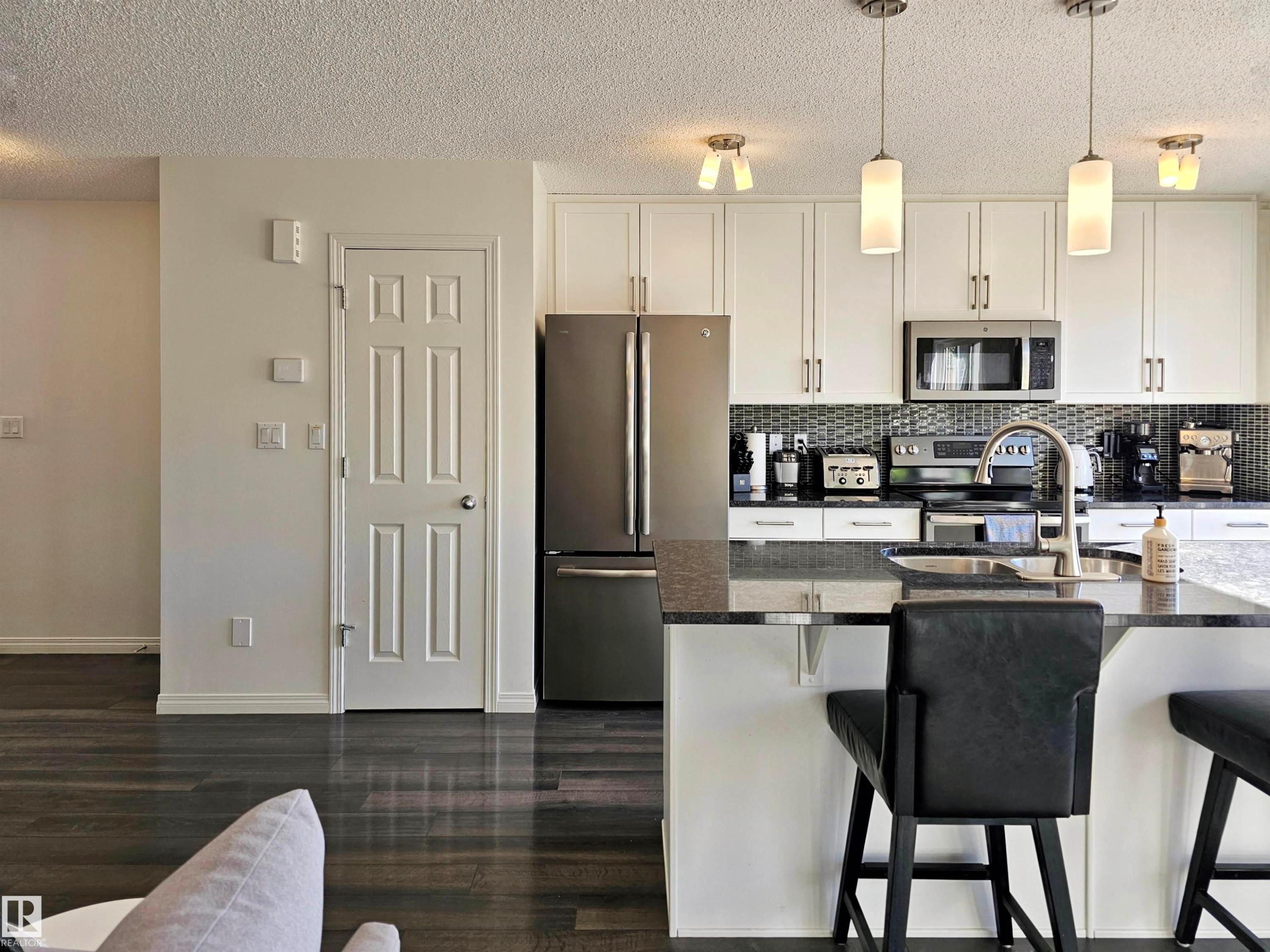 The kitchen features white cabinetry, stainless steel appliances, a dark tile backsplash, and a kitchen island with a sink and pendant lighting - 6888 Evans Wynd, Edmonton, AB - Indoor Photo Showing Kitchen With Stainless Steel Kitchen With Upgraded Kitchen