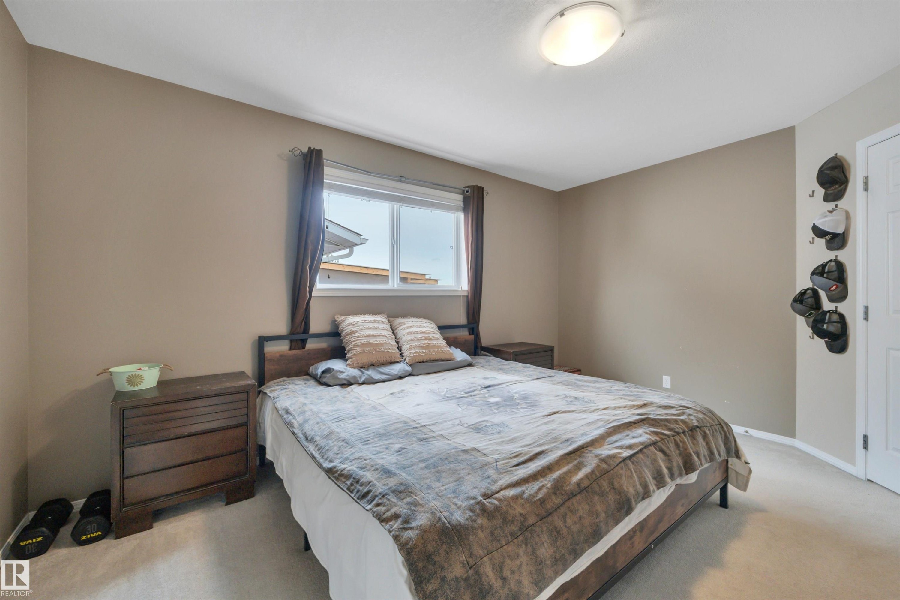 The room features a window with dark curtains, light-colored carpeting, and a ceiling-mounted light fixture - 5 Parkview Crescent, Calmar, AB - Indoor Photo Showing Bedroom