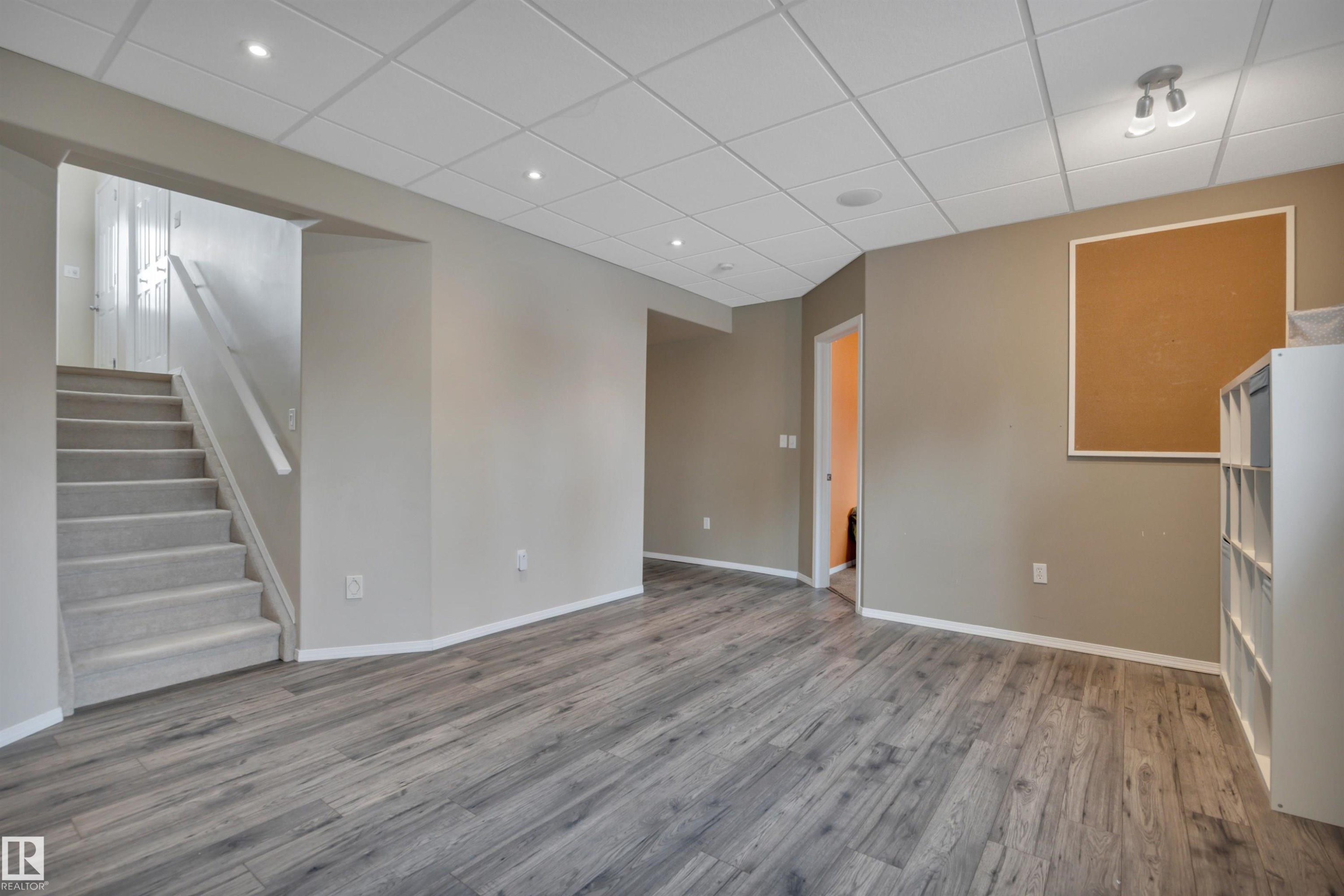 Expansive room featuring wood-look flooring, a drop ceiling with recessed lighting, and a carpeted staircase - 5 Parkview Crescent, Calmar, AB - Indoor Photo Showing Other Room