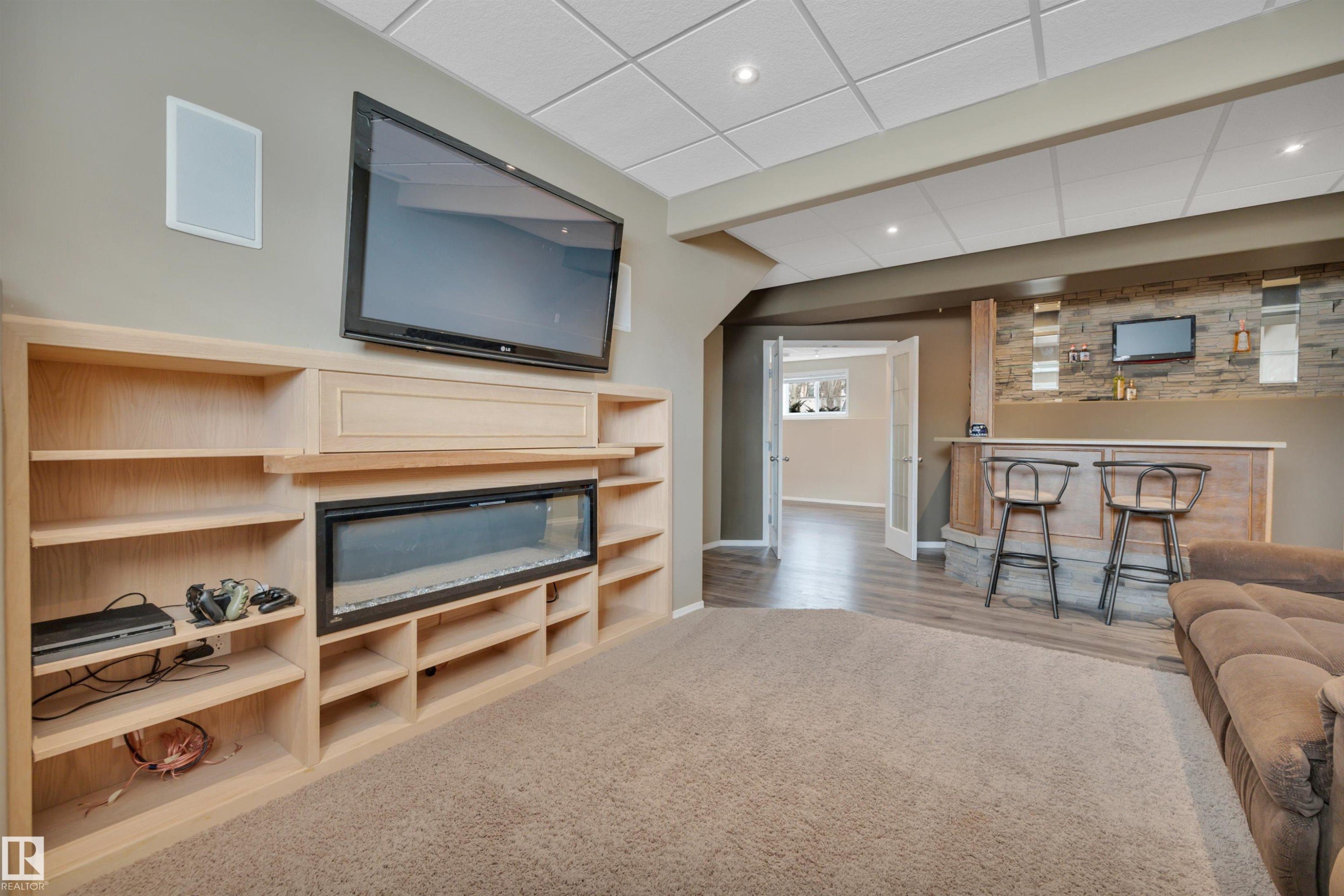 The property features a media wall with built-in shelving and an electric fireplace, set against a backdrop of neutral-toned walls - 5 Parkview Crescent, Calmar, AB - Indoor