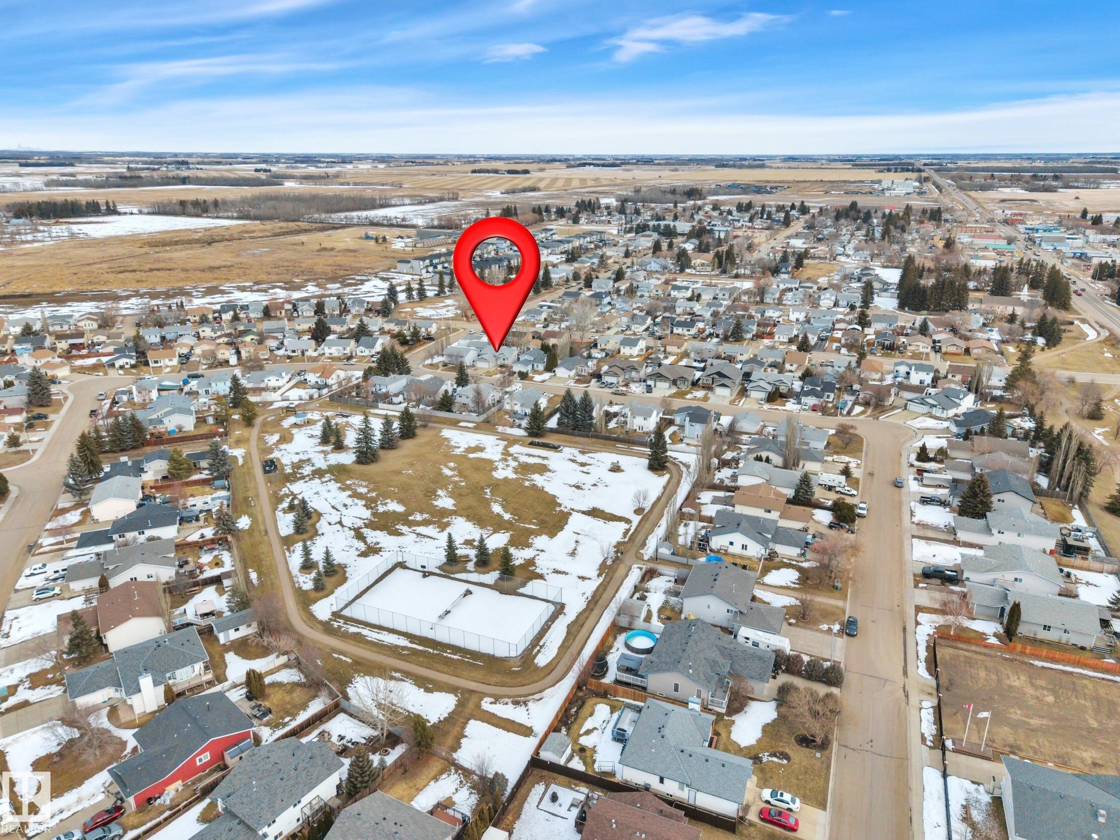Aerial view of the property's setting within a residential area, featuring surrounding homes with various roof styles and a nearby undeveloped lot with some trees and visible patches of snow - 5 Parkview Crescent, Calmar, AB - Outdoor With View