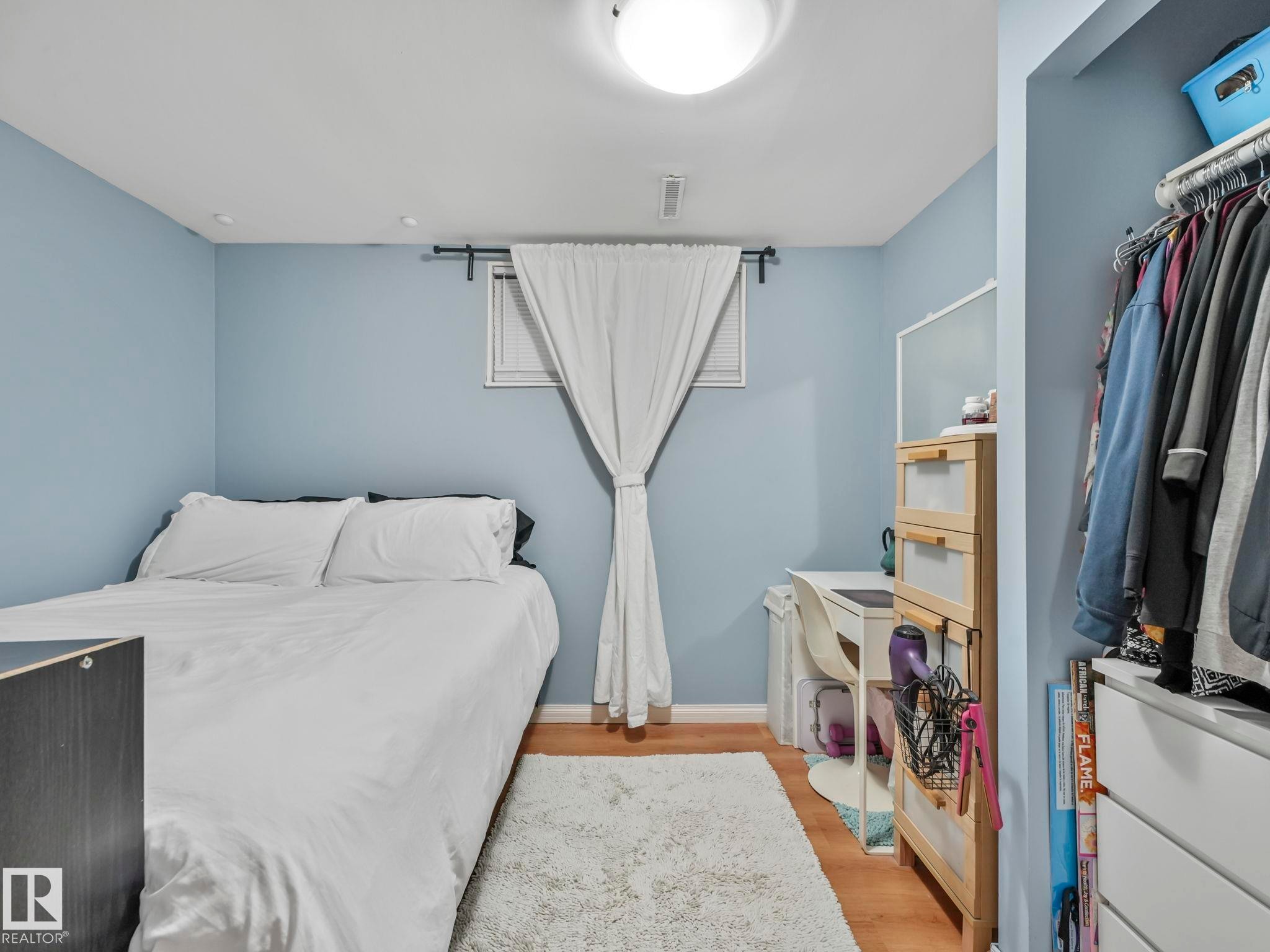 This living space features light blue walls, hardwood flooring, and a window with white curtains - 12141 96 Street, Edmonton, AB - Indoor Photo Showing Bedroom