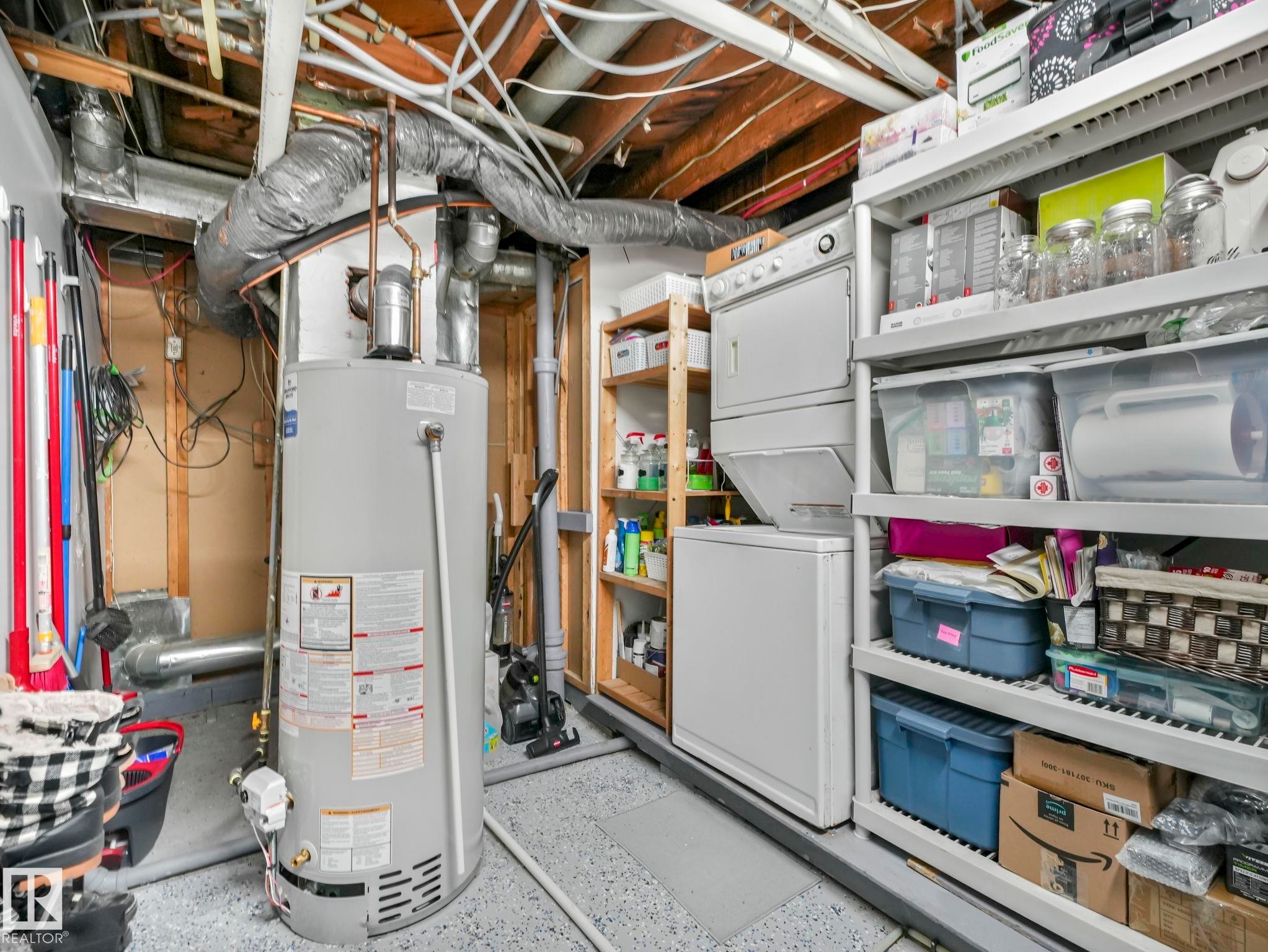 Utility area featuring a water heater, a stackable washer and dryer, and built-in shelving for storage - 12141 96 Street, Edmonton, AB - Indoor Photo Showing Basement