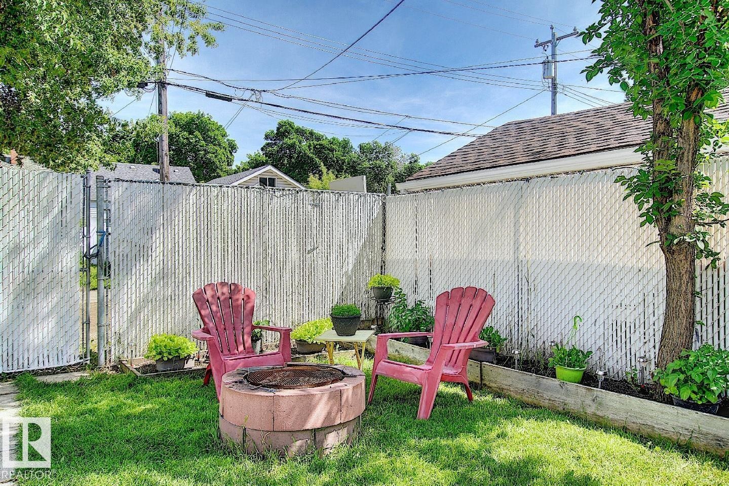 The property features a fenced yard with a lush green lawn, mature trees, and a fire pit - 12141 96 Street, Edmonton, AB - Outdoor