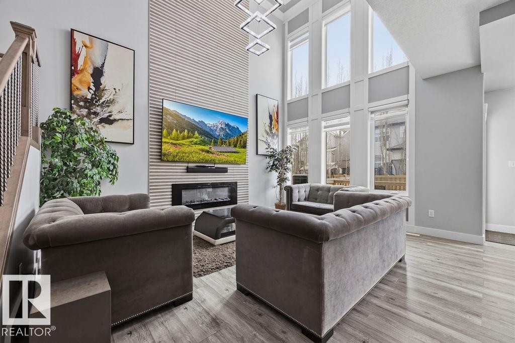This living area features a high ceiling, large windows providing natural light, and light-colored flooring - 17534 60A Street, Edmonton, AB - Indoor Photo Showing Living Room With Fireplace