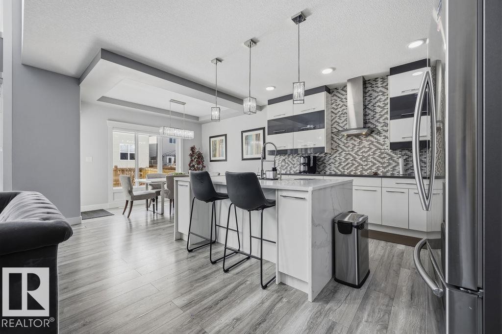 The kitchen features sleek white cabinetry, a stylish patterned backsplash, and stainless steel appliances - 17534 60A Street, Edmonton, AB - Indoor Photo Showing Kitchen With Upgraded Kitchen