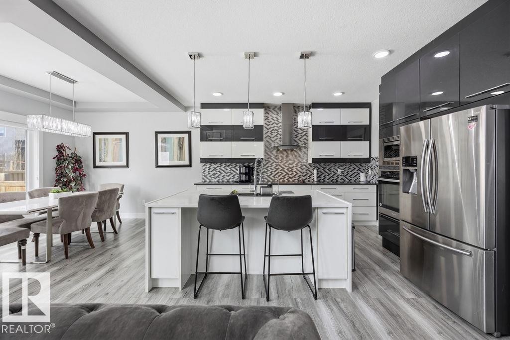 The kitchen features a large island with seating, stainless steel appliances, and a mosaic tile backsplash - 17534 60A Street, Edmonton, AB - Indoor Photo Showing Kitchen With Stainless Steel Kitchen With Upgraded Kitchen