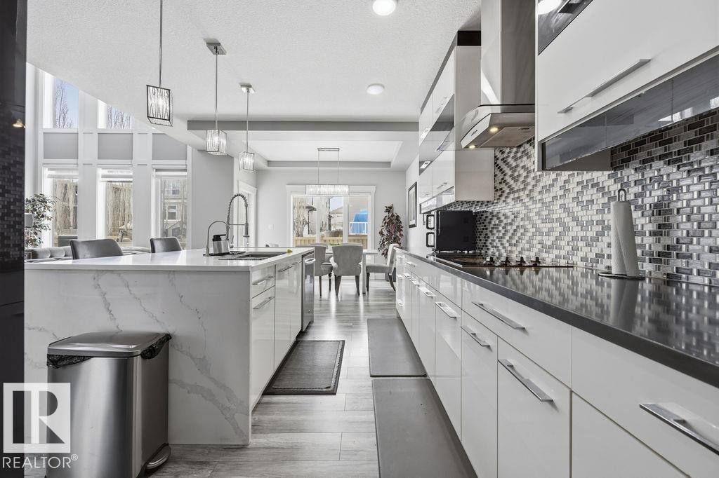 The kitchen features a large island with a sink, white cabinetry, dark countertops, and a striking tile backsplash - 17534 60A Street, Edmonton, AB - Indoor Photo Showing Kitchen With Upgraded Kitchen