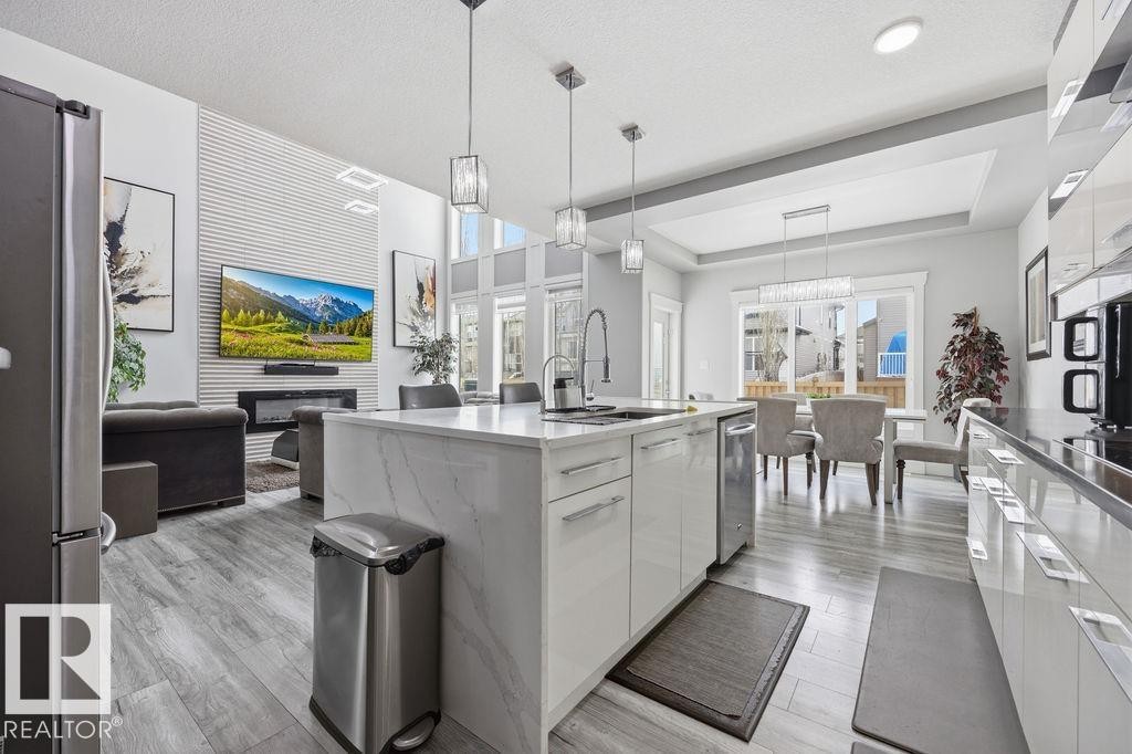 This open-concept living space features light-toned flooring, a kitchen island with a sink and pendant lighting, and a dining area with large windows - 17534 60A Street, Edmonton, AB - Indoor Photo Showing Kitchen With Upgraded Kitchen