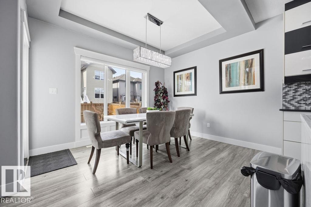 The dining area features engineered hardwood flooring, a modern linear chandelier, and a large window providing natural light - 17534 60A Street, Edmonton, AB - Indoor Photo Showing Dining Room