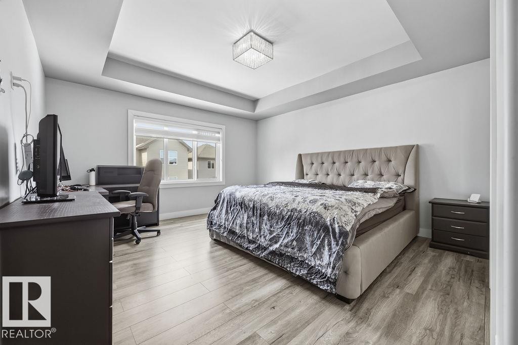 This room features a tray ceiling with a contemporary light fixture, a window providing natural light, and light-toned flooring - 17534 60A Street, Edmonton, AB - Indoor Photo Showing Bedroom