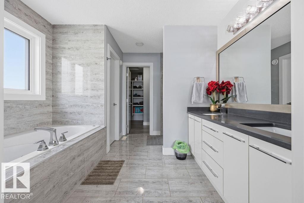 Bathroom featuring a large vanity with dual sinks, a spacious bathtub with tile surround, and tile flooring - 17534 60A Street, Edmonton, AB - Indoor Photo Showing Bathroom