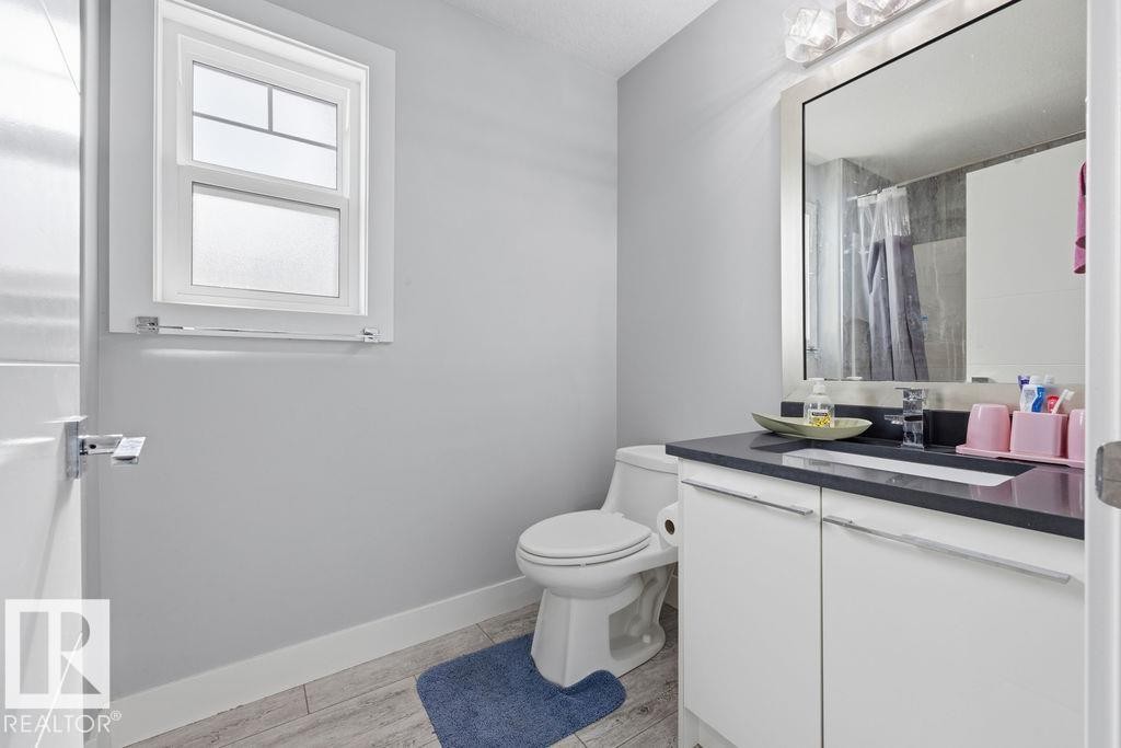 The bathroom features a window, a white toilet, and a vanity with a dark countertop and white cabinetry - 17534 60A Street, Edmonton, AB - Indoor Photo Showing Bathroom