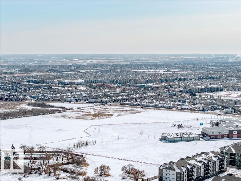 Aerial view showcasing the expansive community, including residential buildings, snow-covered open fields, and trees - 17534 60A Street, Edmonton, AB - Outdoor With View