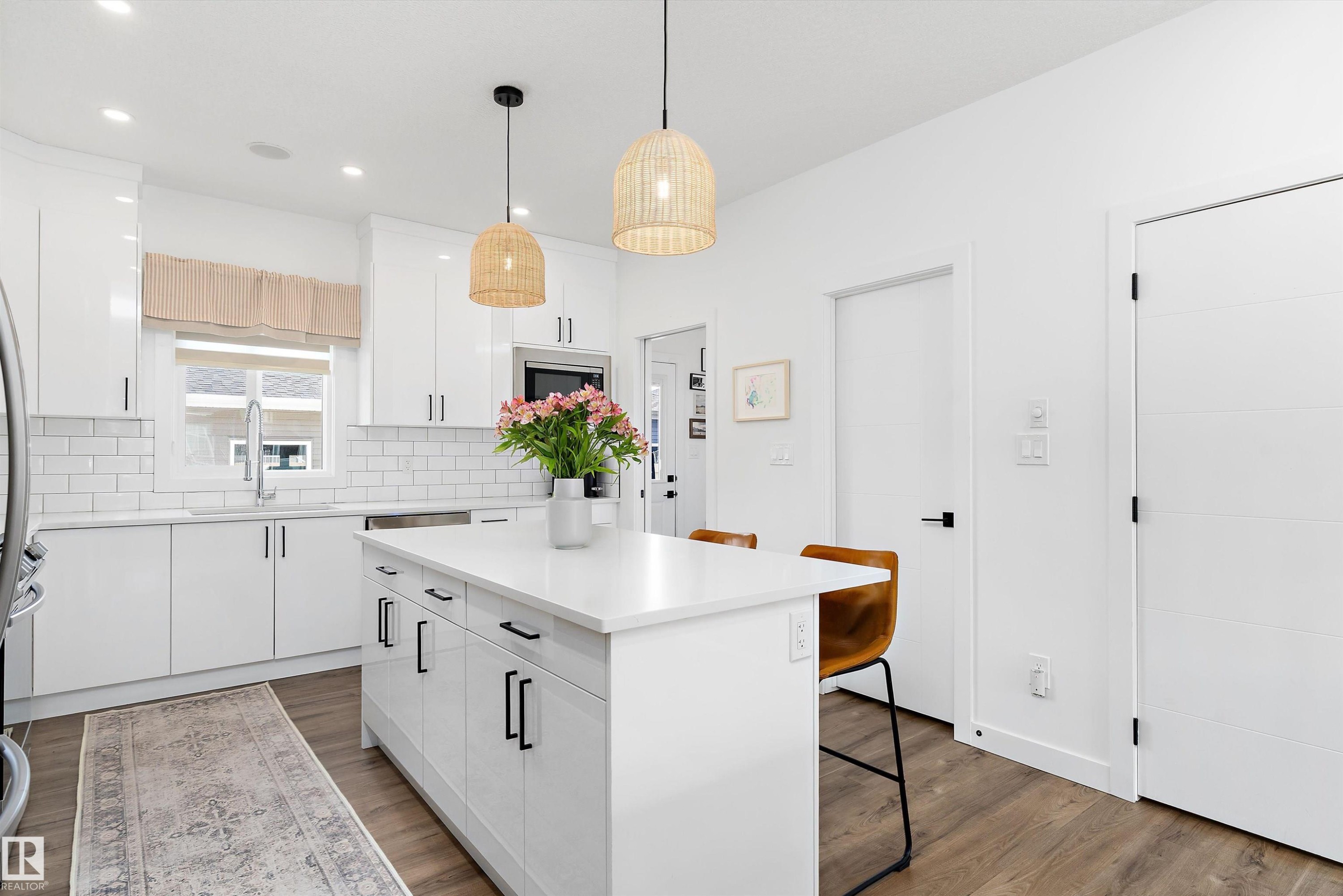 The kitchen features a large island with a white countertop and seating for two, white cabinetry with black hardware, and wood flooring - 1305 Enright Landing, Edmonton, AB - Indoor Photo Showing Kitchen With Upgraded Kitchen