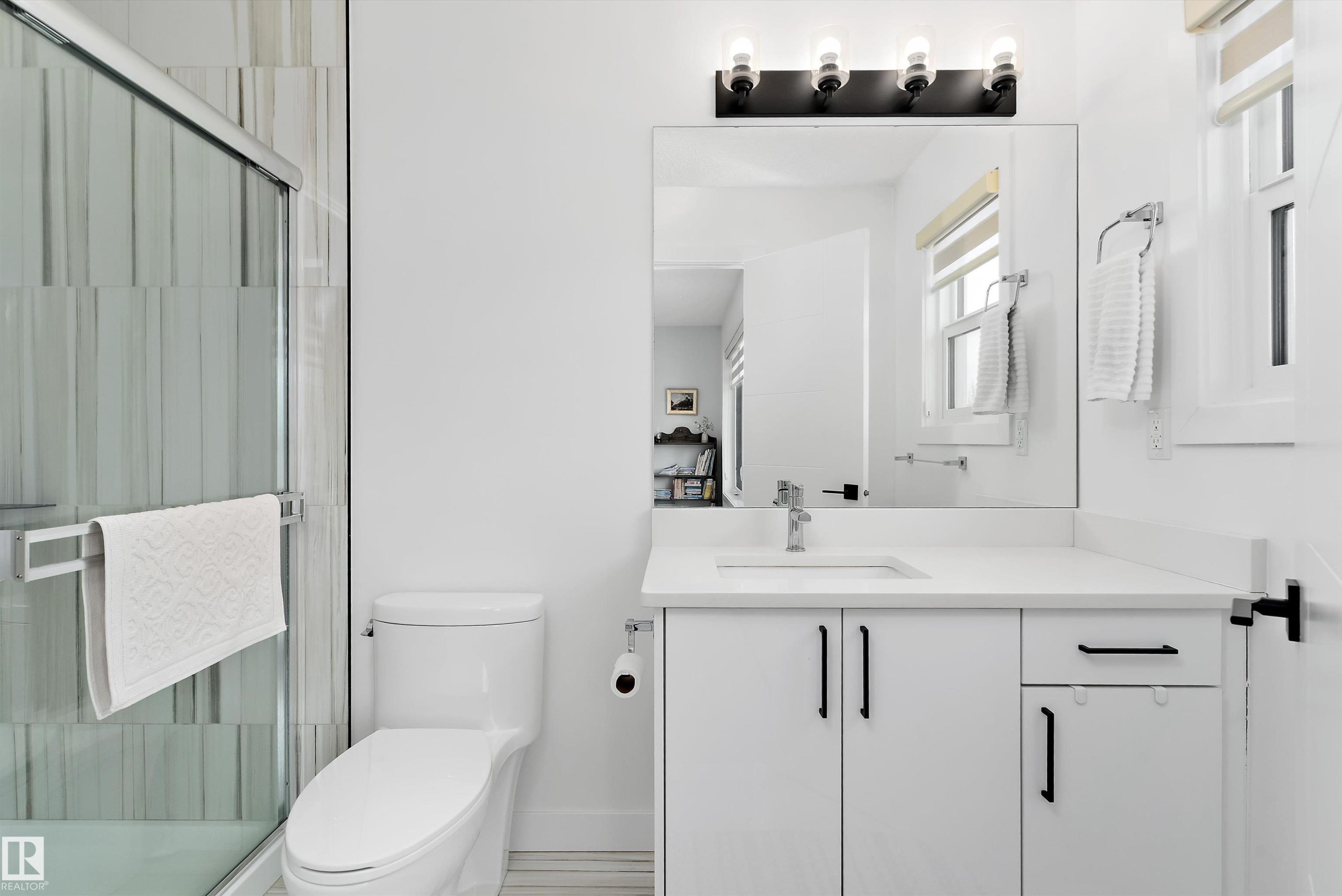 The bathroom features a modern vanity with a white countertop and dark-colored pulls, a large mirror, and an enclosed shower with a glass door - 1305 Enright Landing, Edmonton, AB - Indoor Photo Showing Bathroom