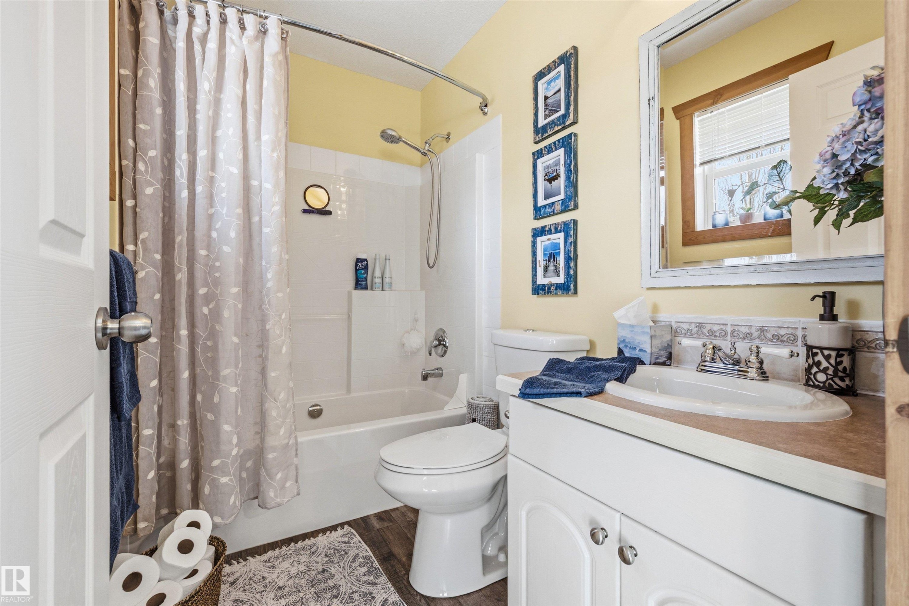 Bathroom featuring a white vanity with a built-in sink, a toilet, a bathtub with an overhead shower, and a decorative mirror - 17 Sunset Harbour, Rural Wetaskiwin County, AB - Indoor Photo Showing Bathroom