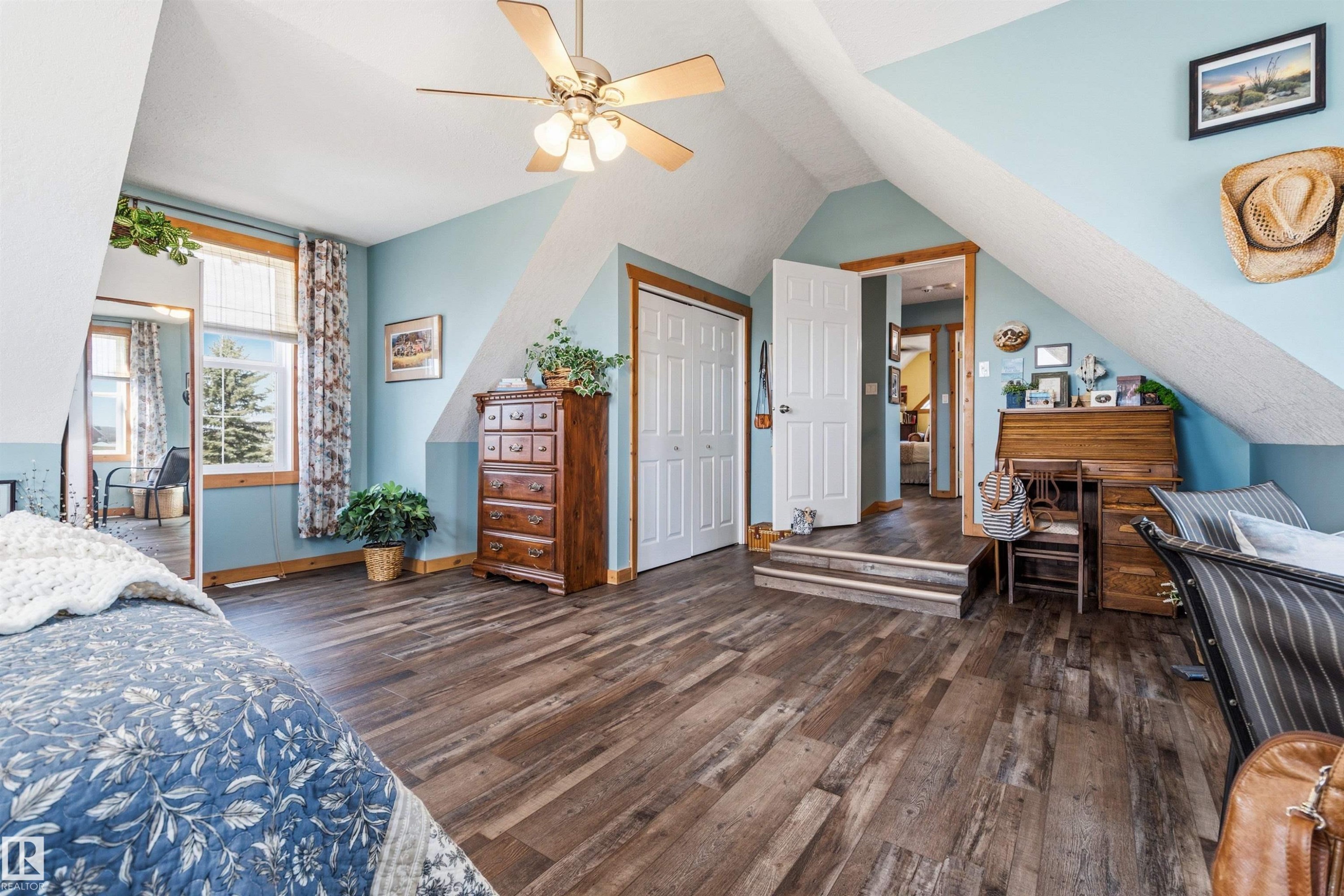 The property features wood-look flooring, sloped ceilings, a ceiling fan with integrated lighting, and a window with a view of greenery - 17 Sunset Harbour, Rural Wetaskiwin County, AB - Indoor Photo Showing Bedroom